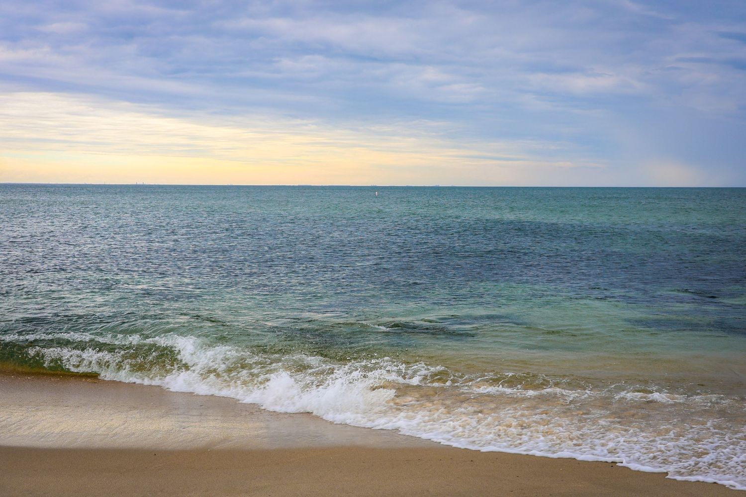 Calm ocean waves gently washing onto a sandy beach at sunset with turquoise water and a colorful sky.