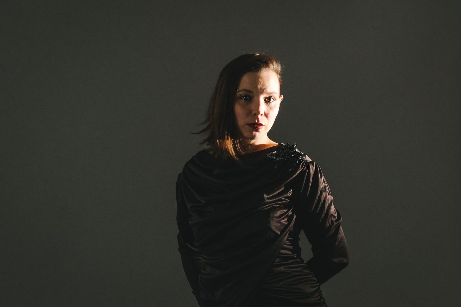 A person with long brown hair poses against a dark background in a dramatic black and white portrait series.