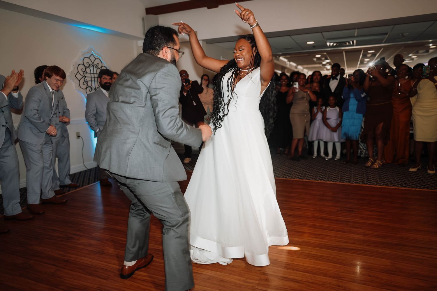 Bride in white gown and groom in gray suit share energetic first dance at wedding reception.