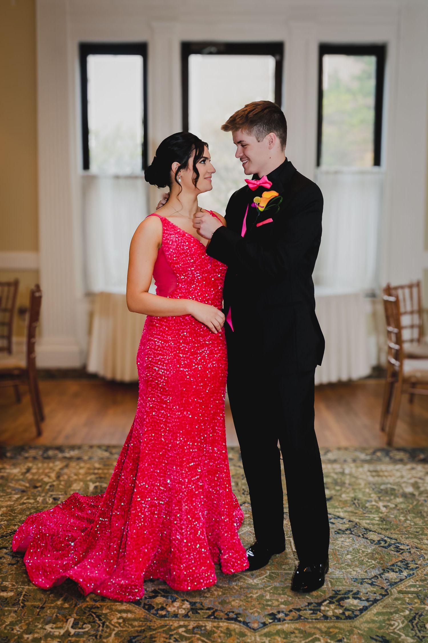 A couple in formal attire, woman in red sequin gown and man in black tuxedo, posing together at prom.