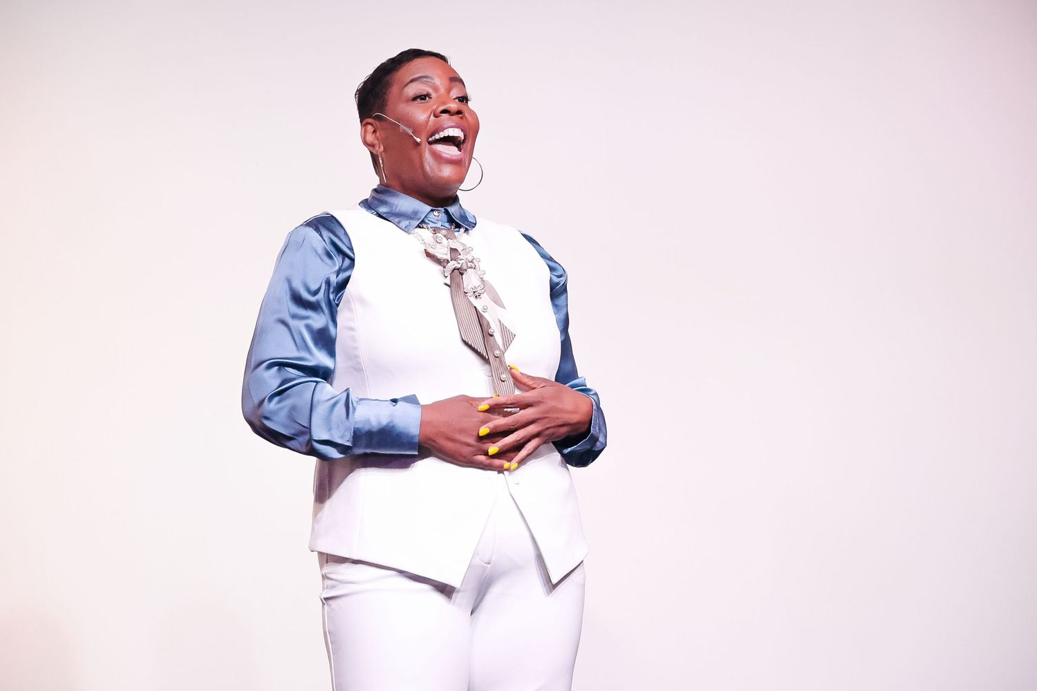 Joyful person in white vest and blue shirt with tie, laughing against a light background.