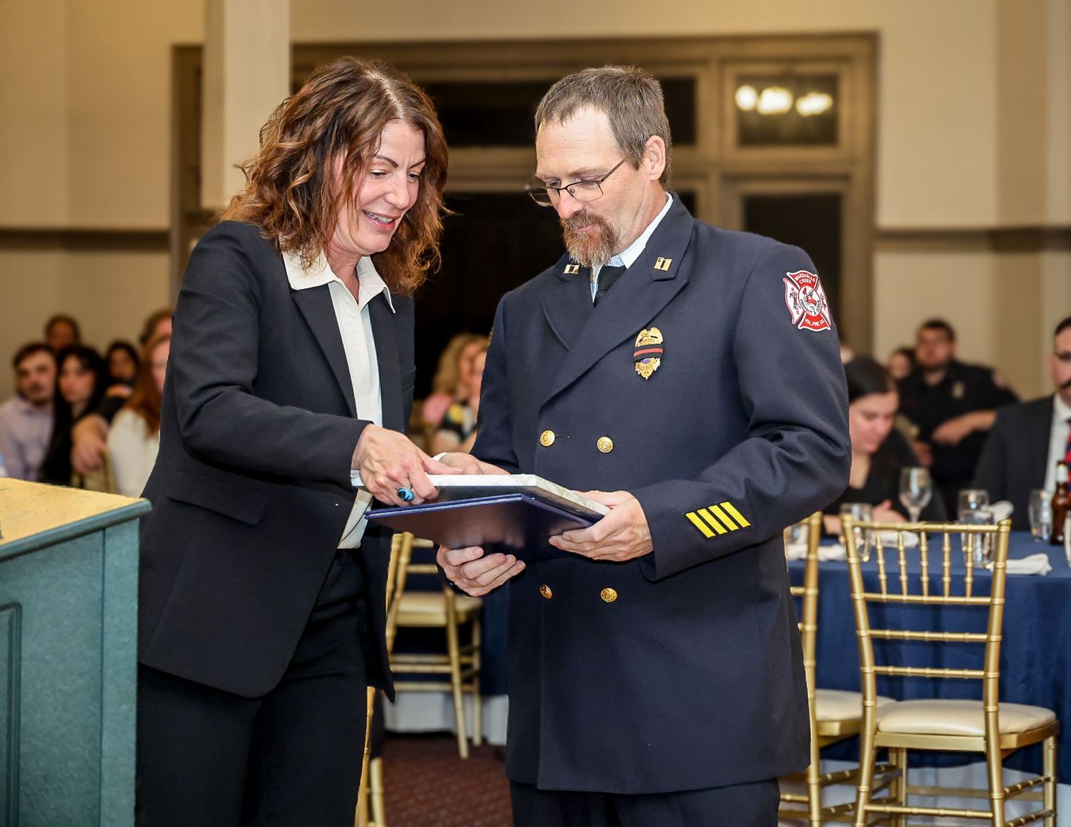 Woman and fire chief reviewing documents together at formal awards ceremony in elegant banquet hall.