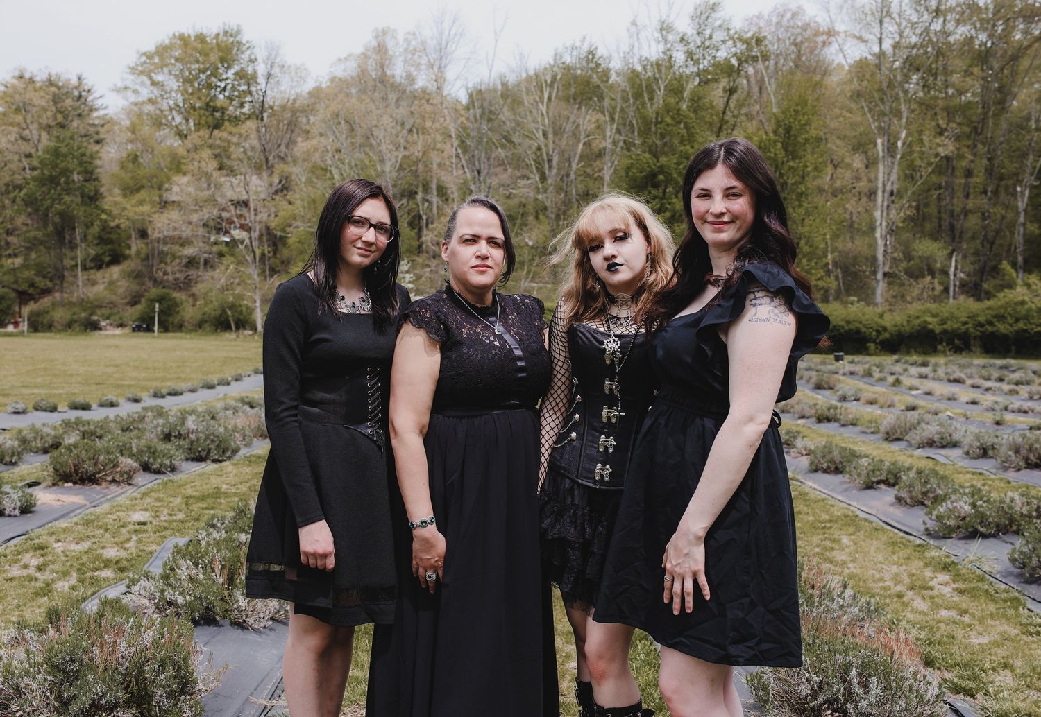 A group wearing black outfits poses together in a garden setting with lavender plants and trees in the background.