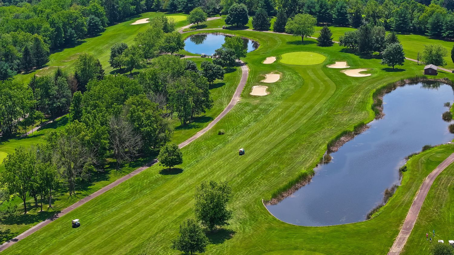 Aerial panoramic view of a lush green golf course with multiple holes, water hazards, and tree-lined fairways.