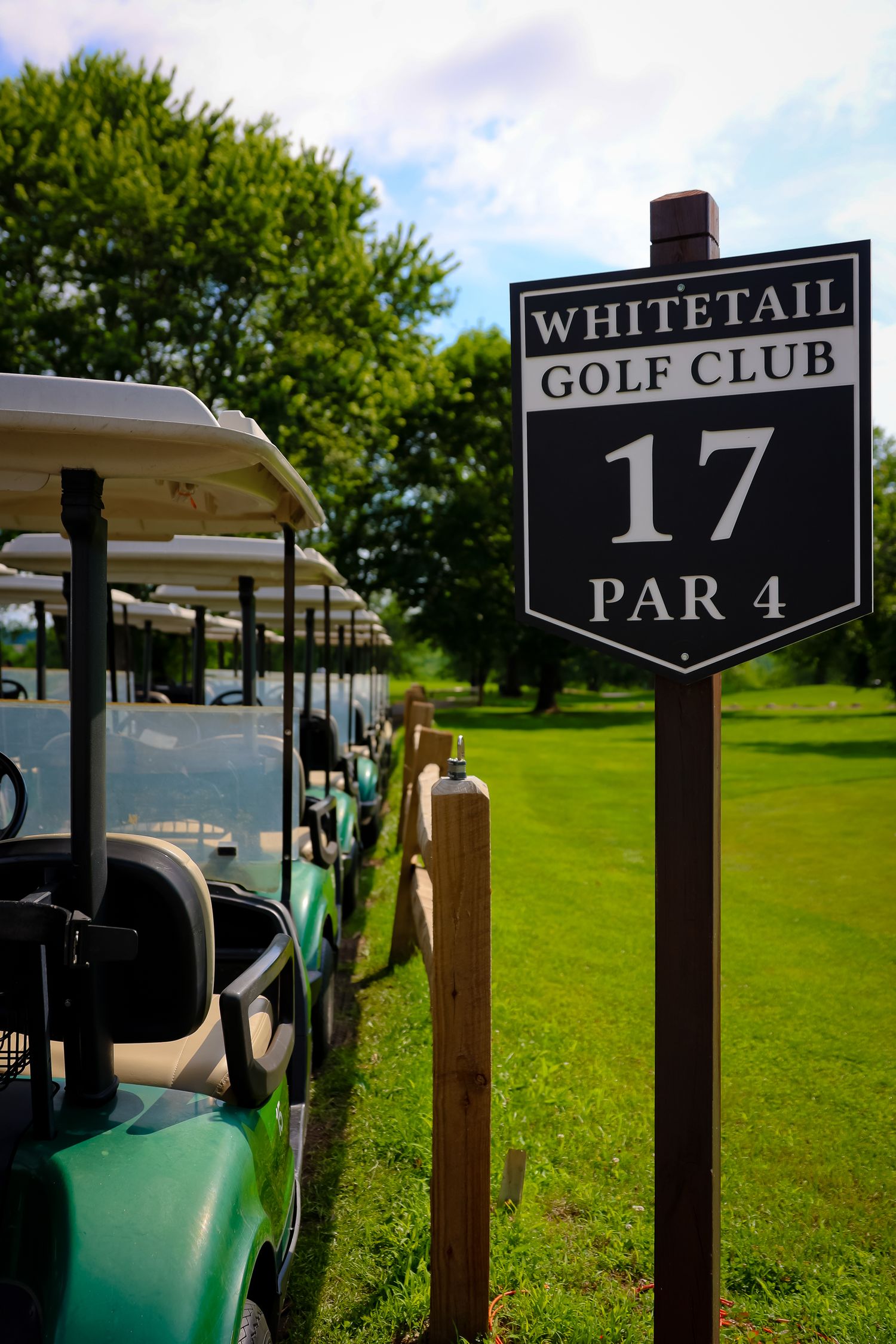 Golf course signs showing hole numbers and par information next to golf carts on a lush green course.