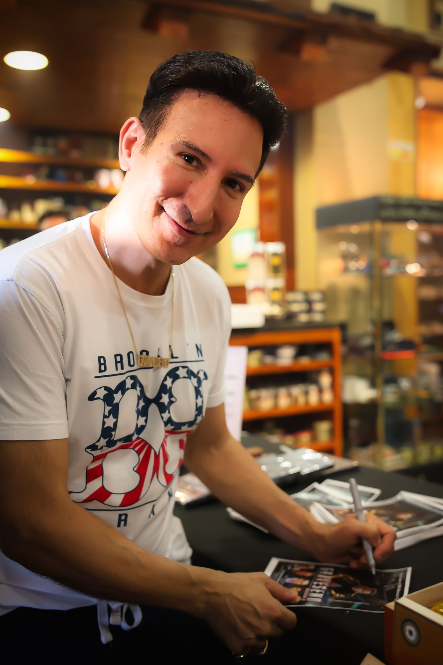 A person wearing a Brooklyn t-shirt sits at a table looking down at some items in front of them.