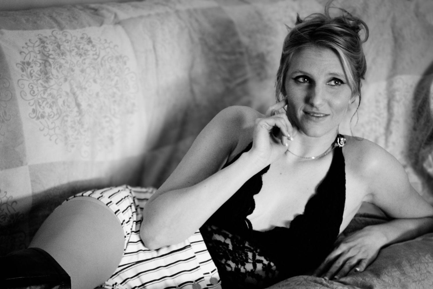 Black and white boudoir photo showing someone reclining on couch in lace lingerie.