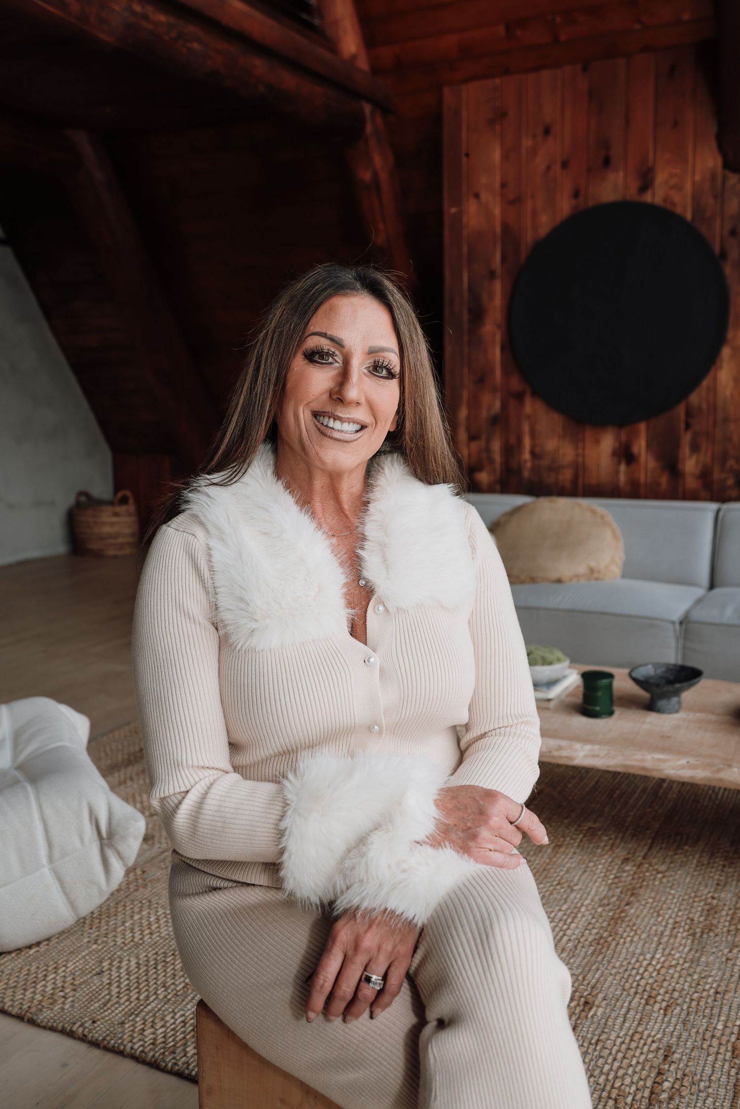 A person in a cozy white sweater sits on a beige carpet in a rustic wooden room.