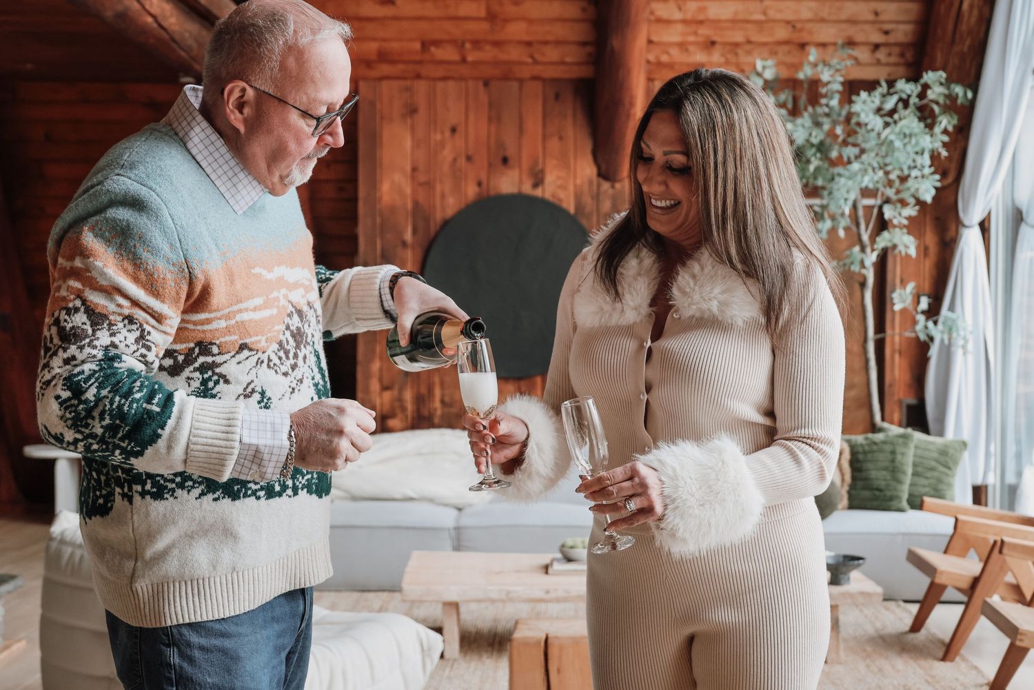 Two people share a warm moment while pouring drinks at a rustic wooden venue decorated with floral arrangements.