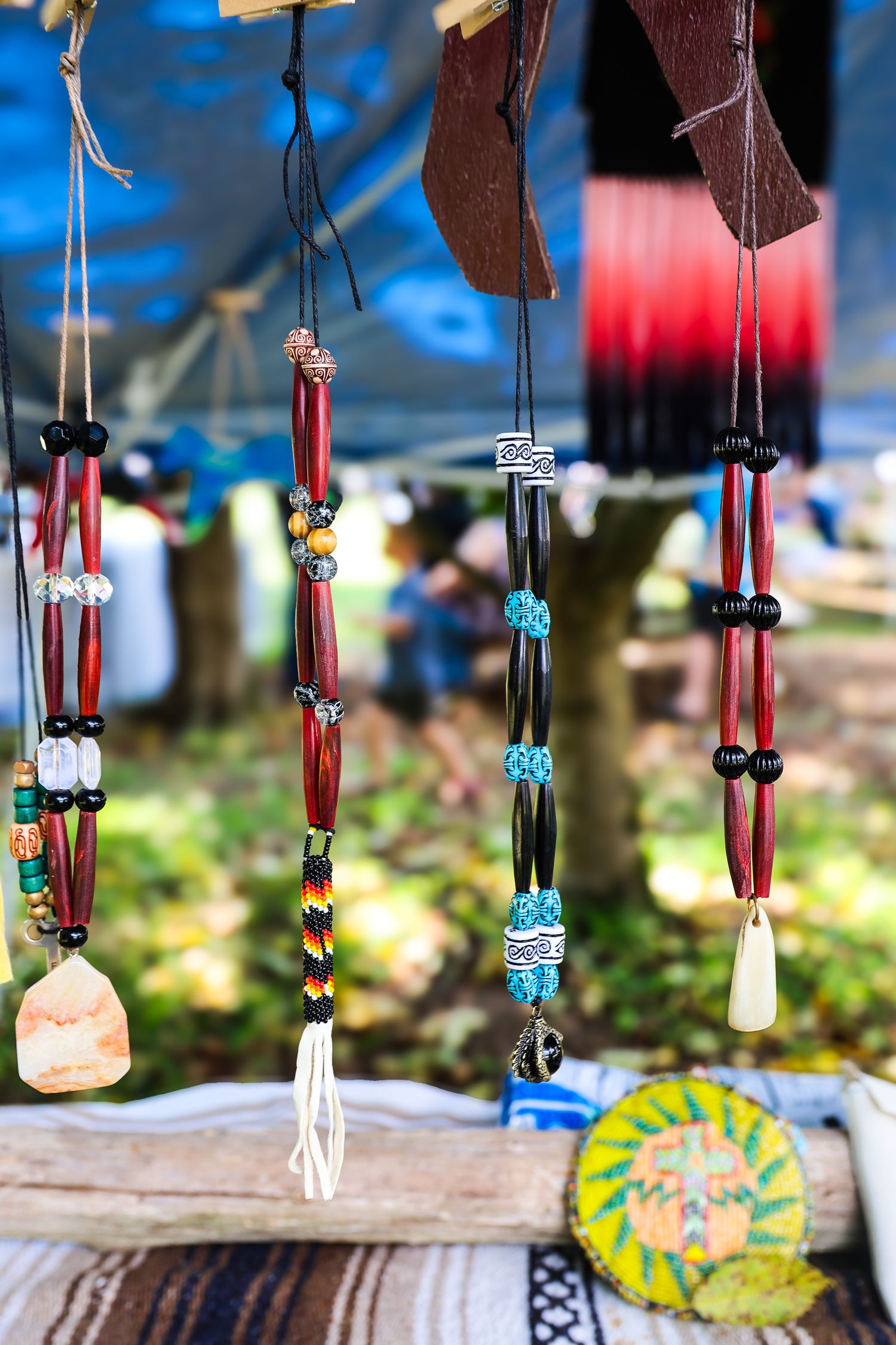 Colorful handmade beaded necklaces with stones and shells hanging at an outdoor craft market display against a blue sky.
