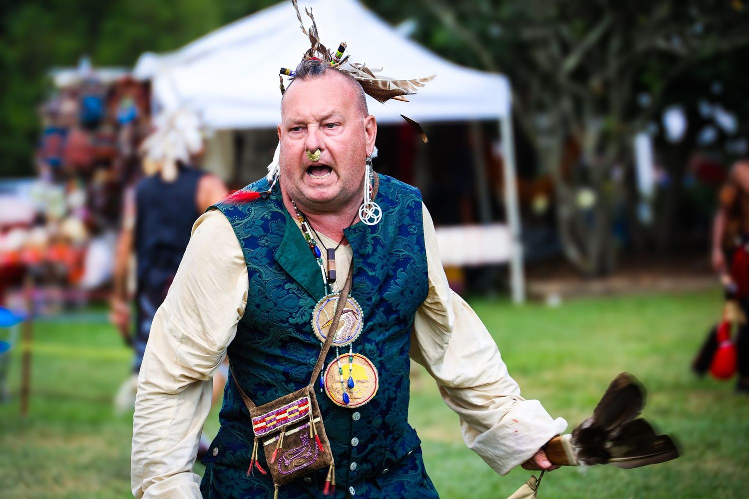 A performer in medieval costume holds a sword while demonstrating theatrical combat moves at a historical reenactment event.