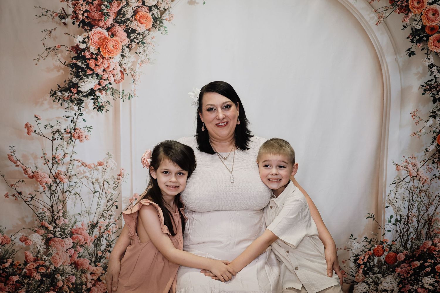 A family poses together against an arched backdrop decorated with delicate coral-colored floral arrangements and greenery.