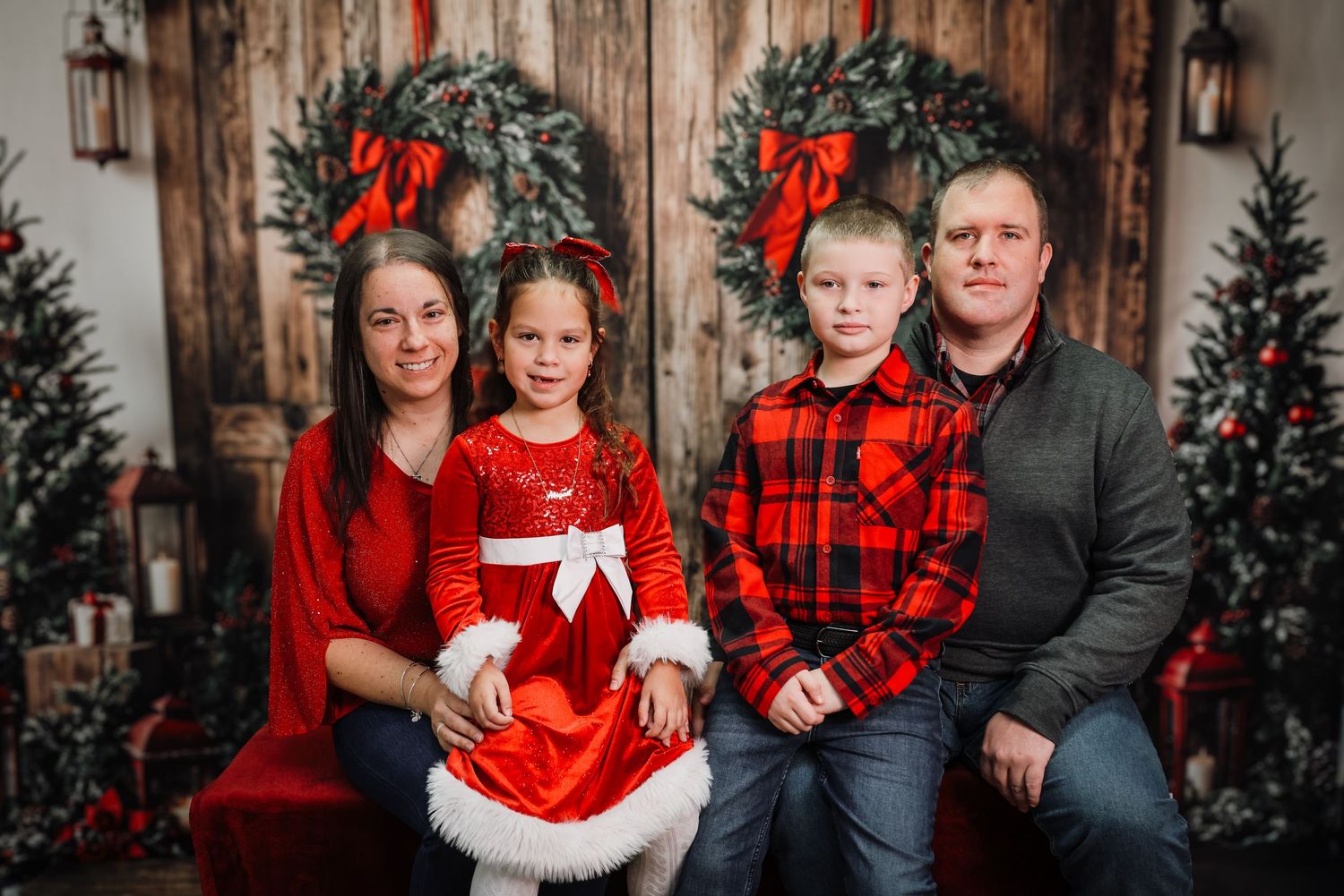 Family wearing coordinating red and black buffalo plaid outfits poses for Christmas photos with decorated tree.