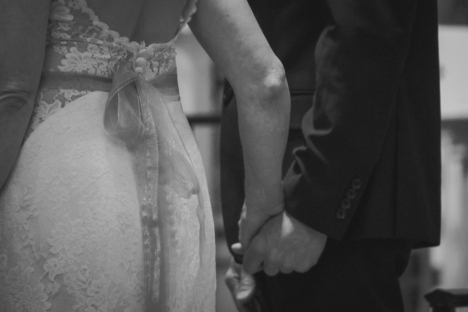 Black and white close-up of a bride and groom holding hands during their wedding ceremony.