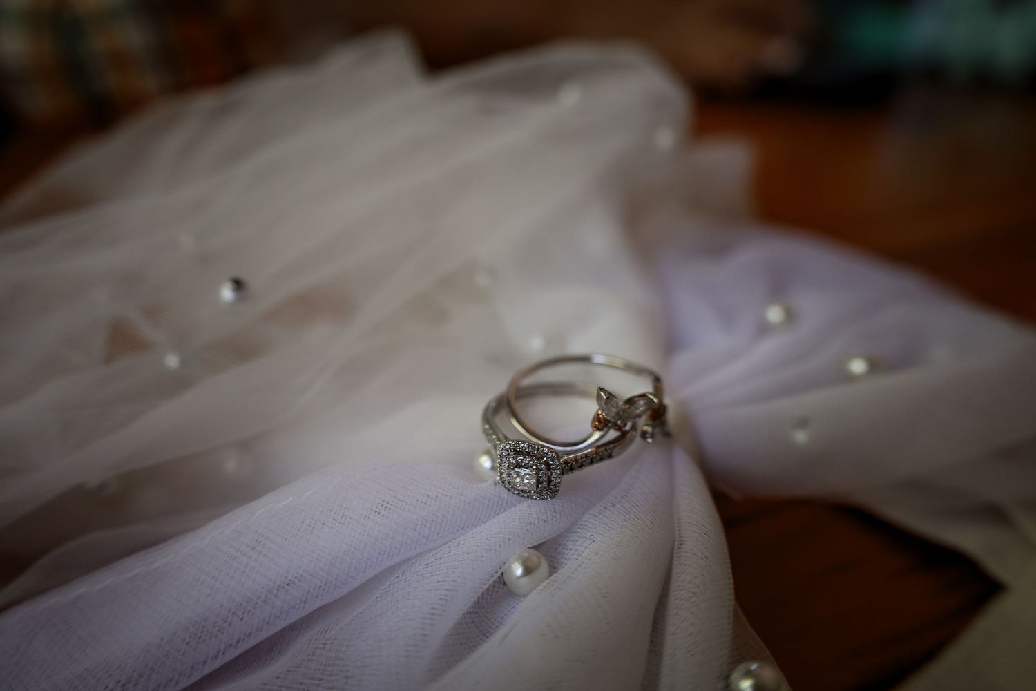 A close-up view of a diamond engagement ring resting on white tulle fabric in soft lighting.