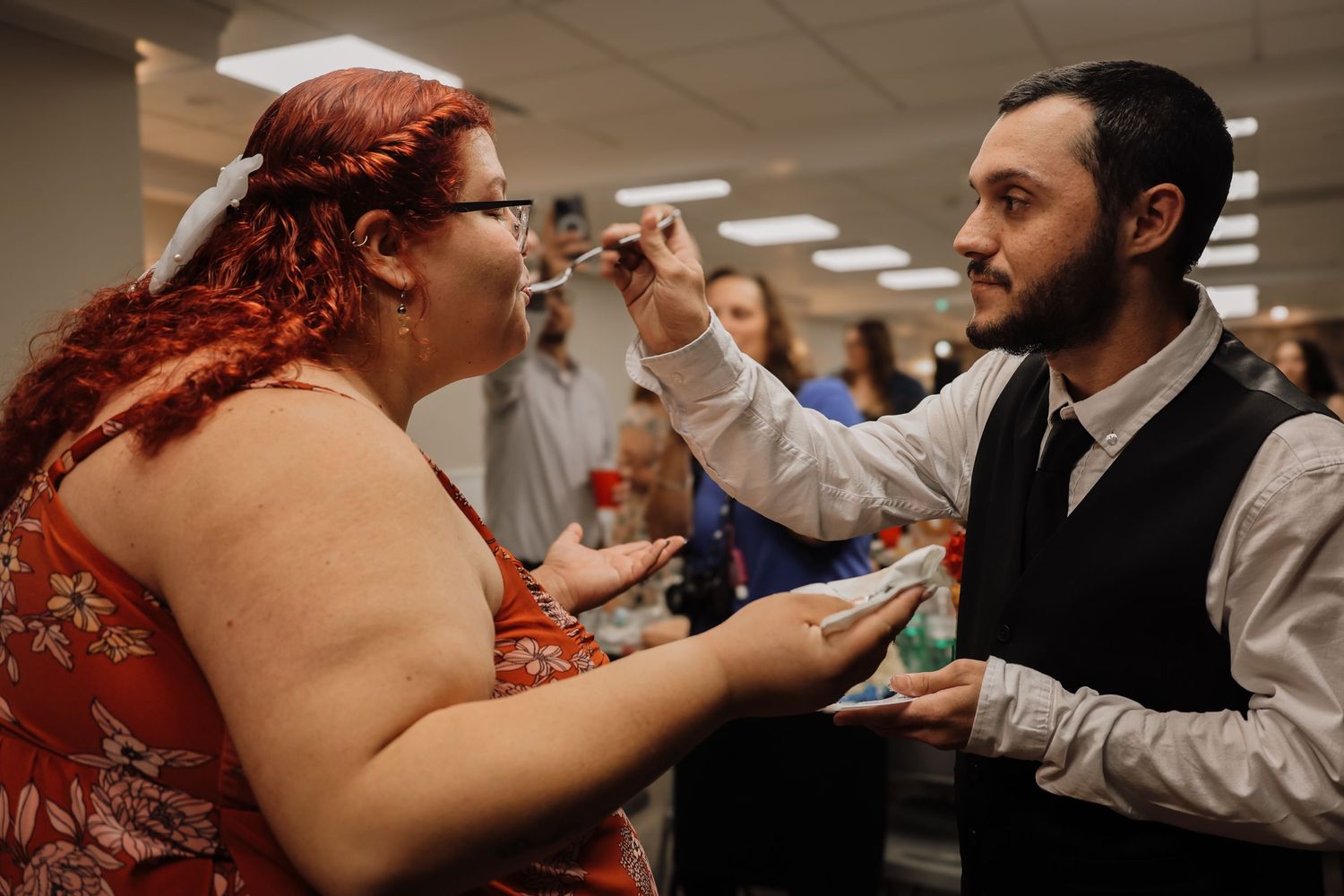 Two people playfully interact at a casual indoor gathering while others look on in the background.