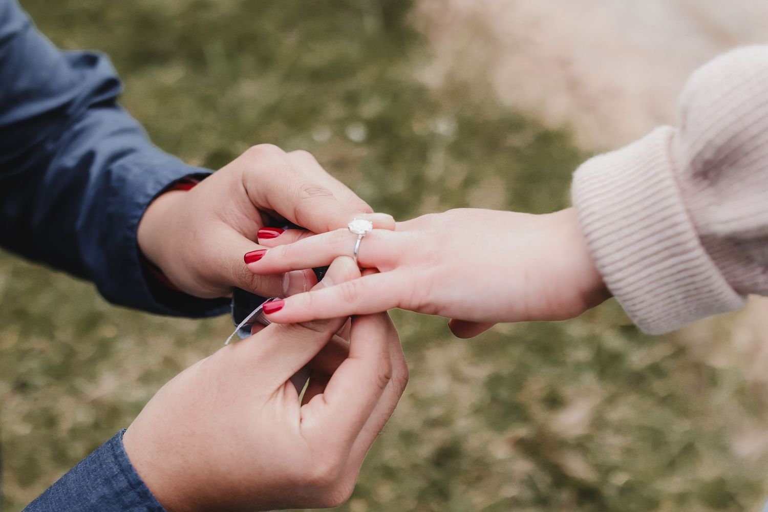 Close up of hands placing engagement ring on finger during romantic outdoor proposal.