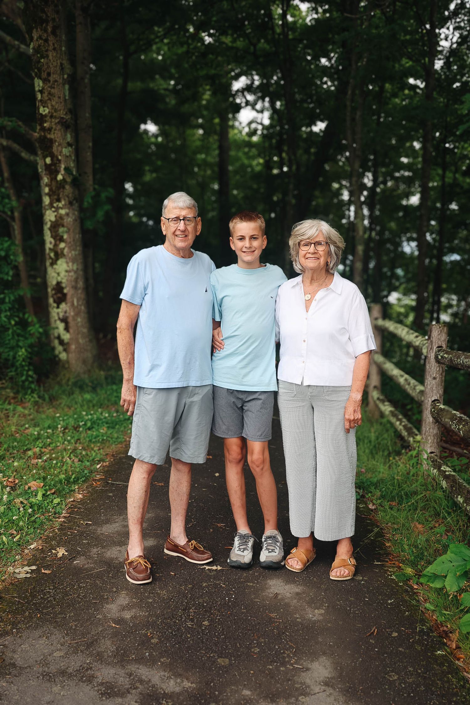 Grandparents smiling with teenage grandson on a tree-lined path.