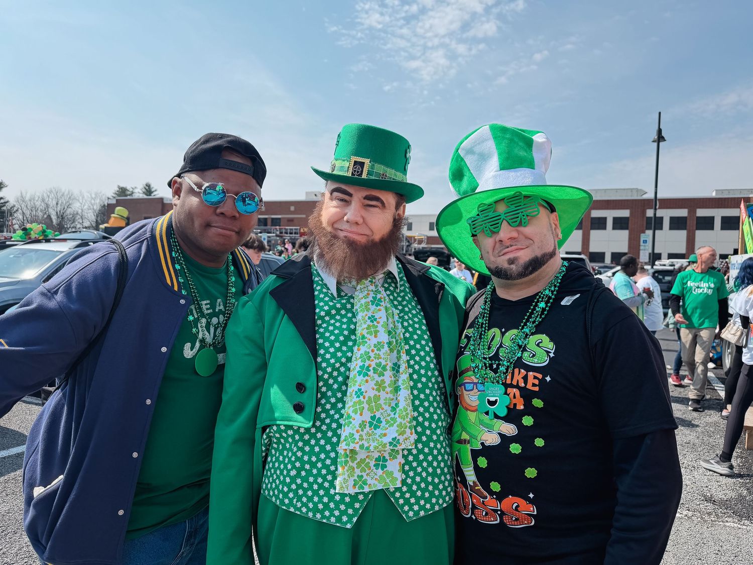 Three friends dressed in festive green St. Patrick's Day costumes pose together outdoors at a parade celebration.