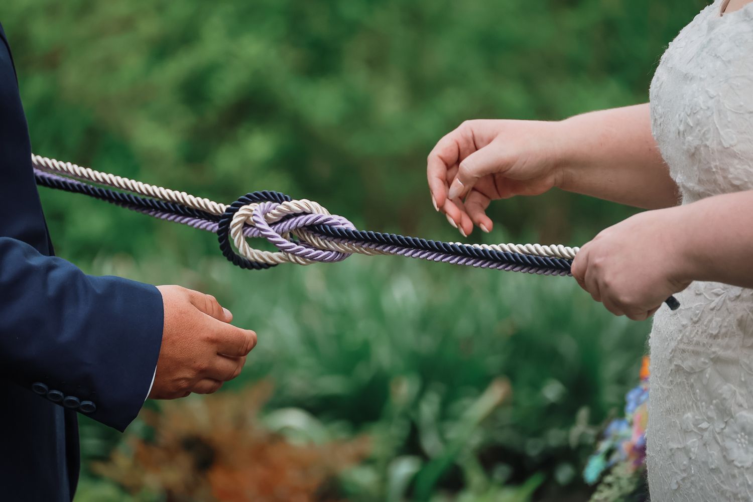 Couple holding a twisted rope knot during a wedding unity ceremony outdoors.