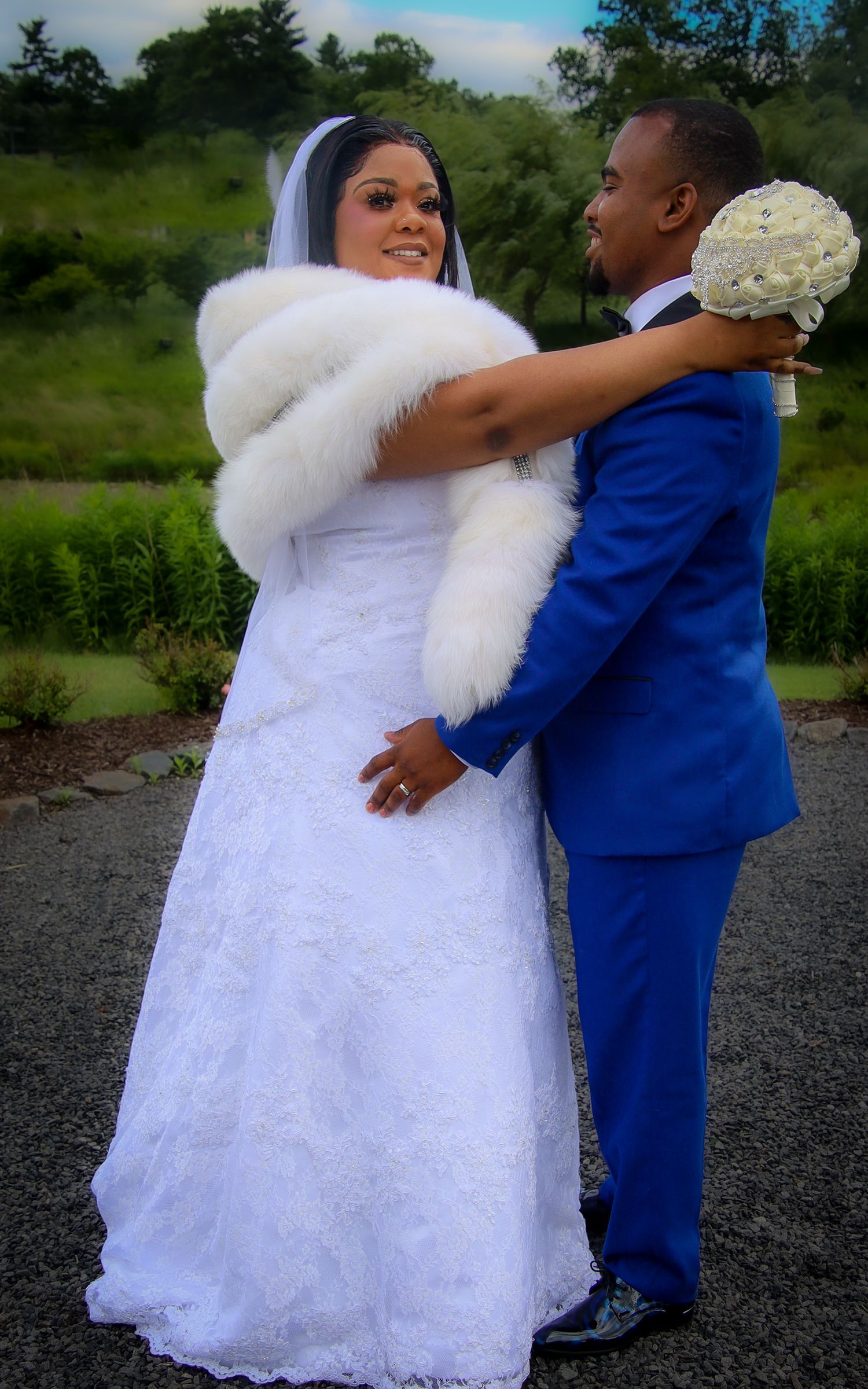 A couple shares a romantic moment in wedding attire, with the bride in white and groom in royal blue outdoors.