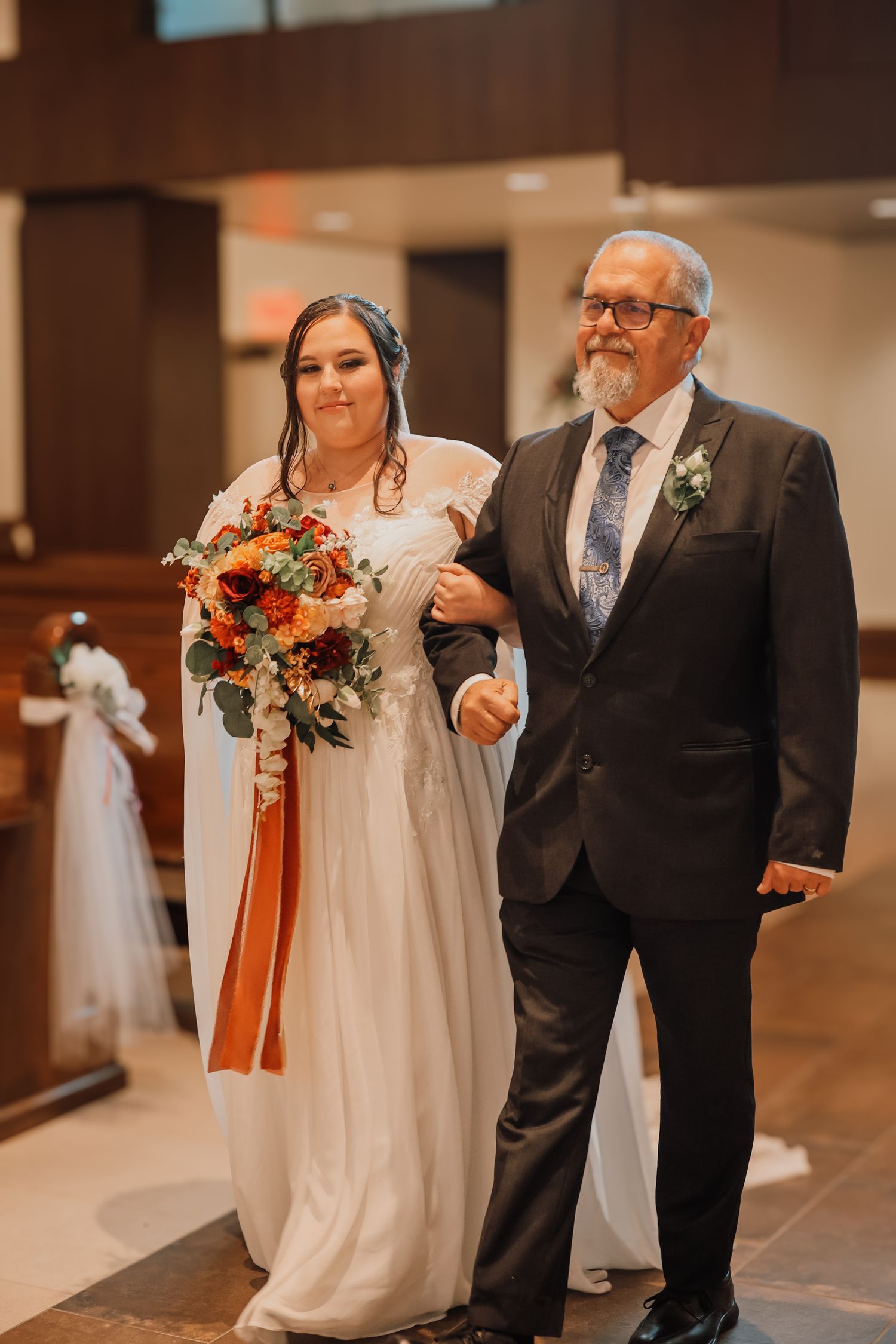 A wedding ceremony processional in a church with a bride in white dress walking down the aisle with her escort.