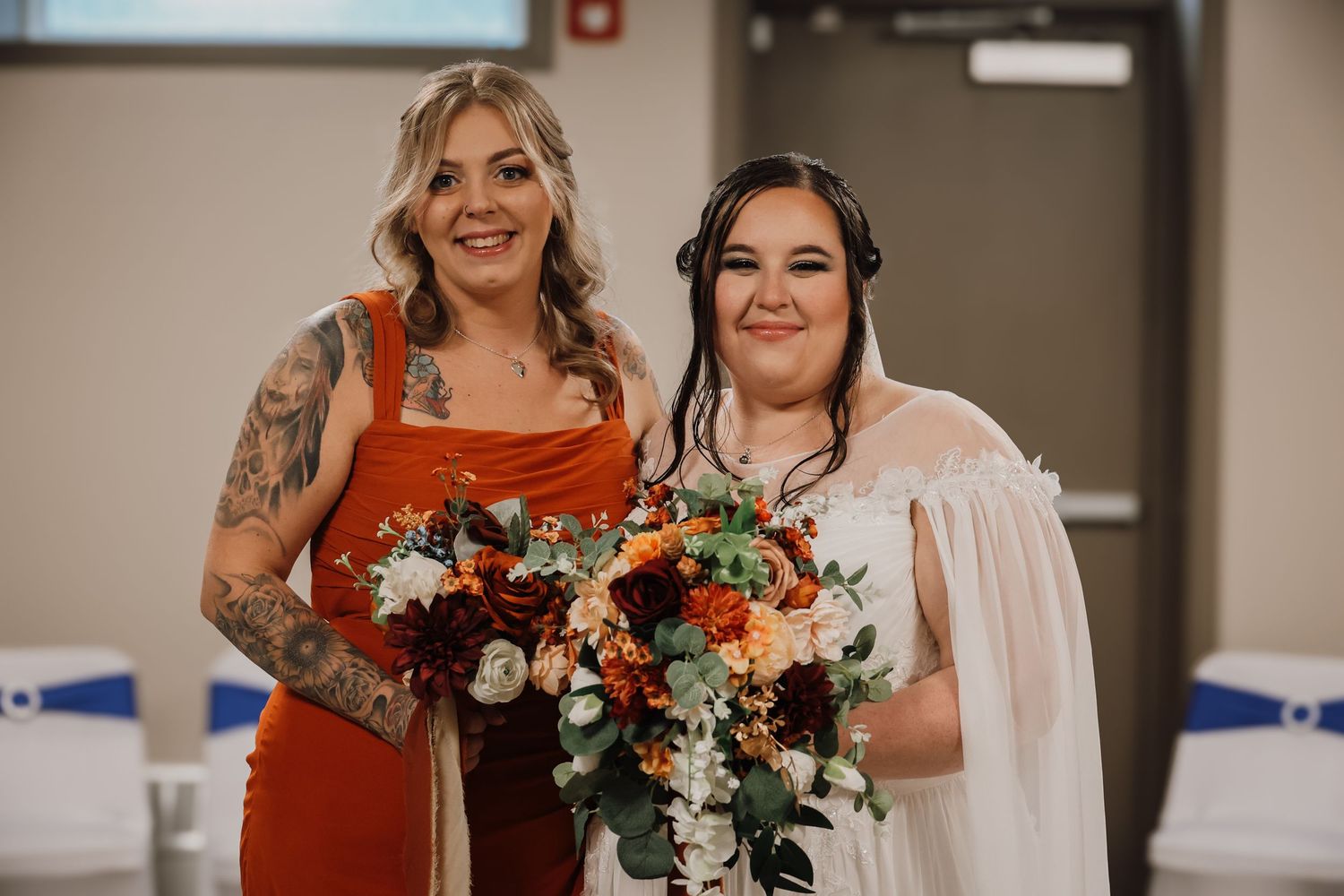 Wedding party members in rust-colored dresses and white gowns pose with vibrant orange and white floral bouquets.