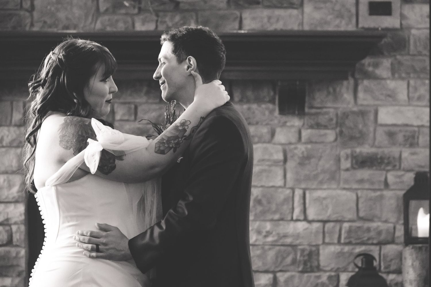 A couple shares romantic dance poses in front of a rustic brick wall.