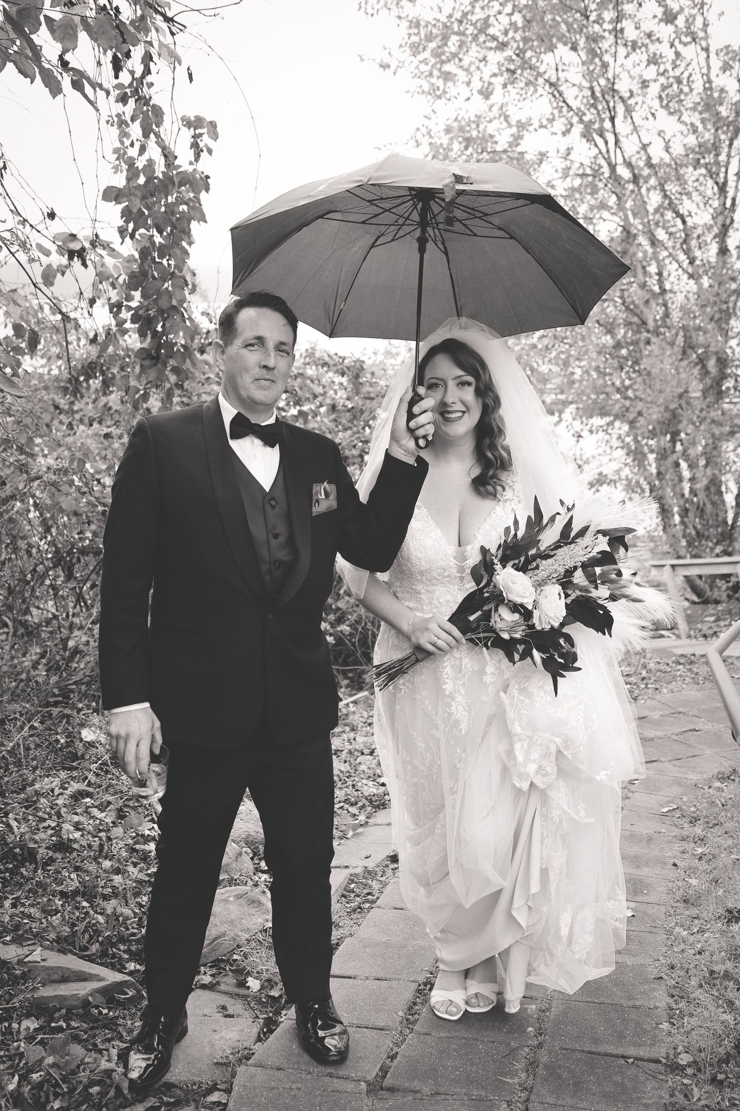 Black and white wedding photos show couple walking together under an umbrella in the rain on their special day.