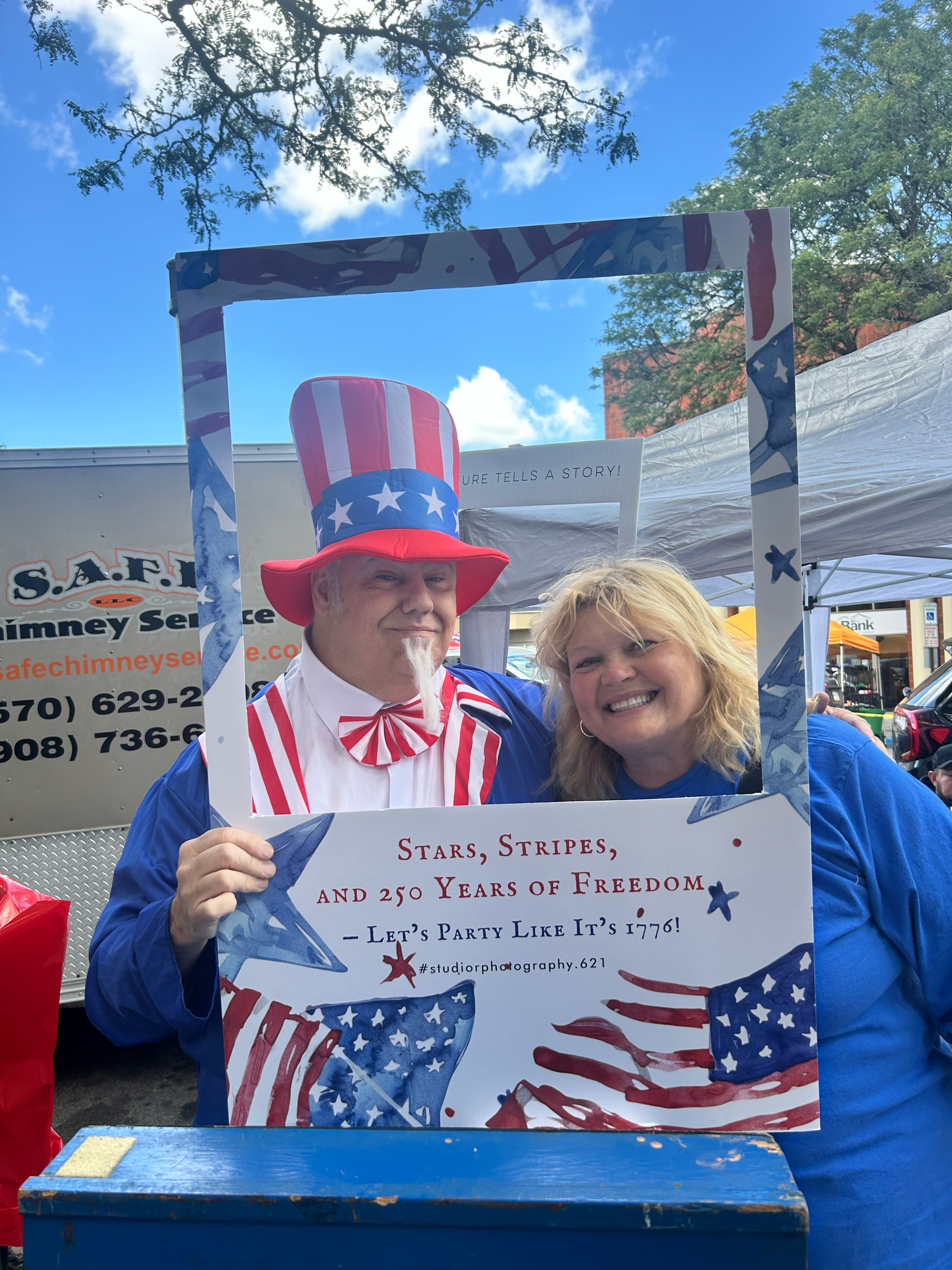 Two people at an outdoor event display a patriotic book about stars and stripes while wearing red white and blue attire.