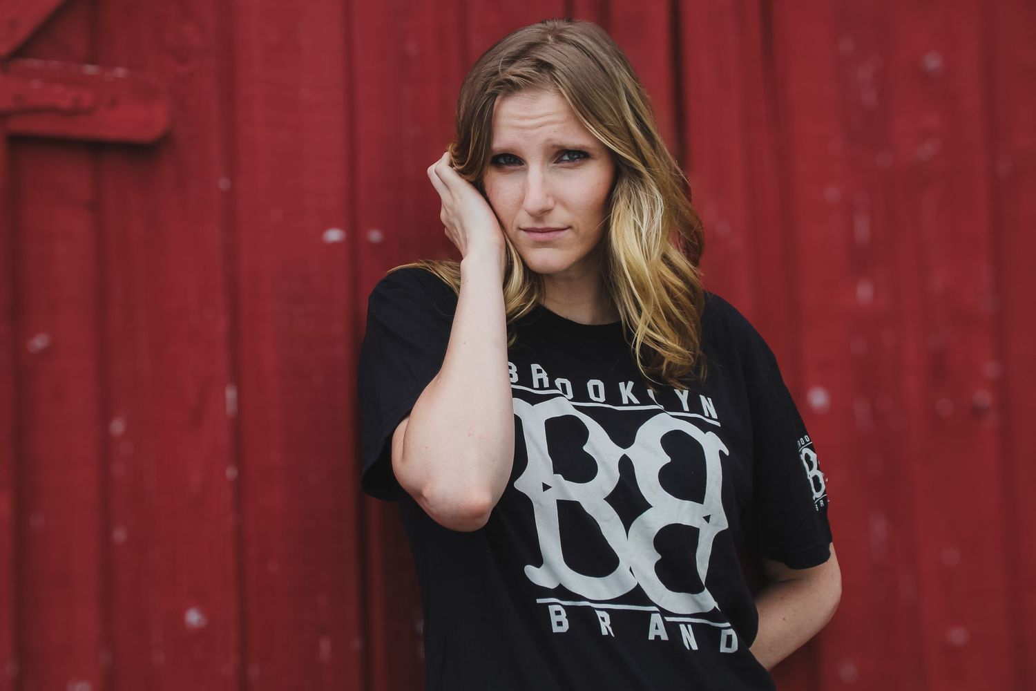 Woman in black t-shirt poses in front of red barn wall with natural lighting.