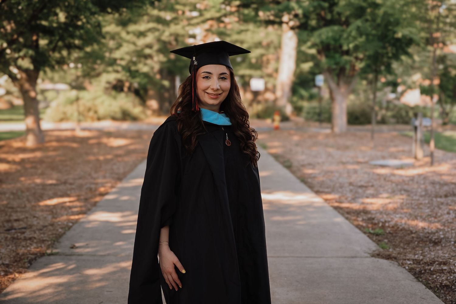 Graduate in cap and gown poses outdoors for graduation photos in a park setting during golden hour.