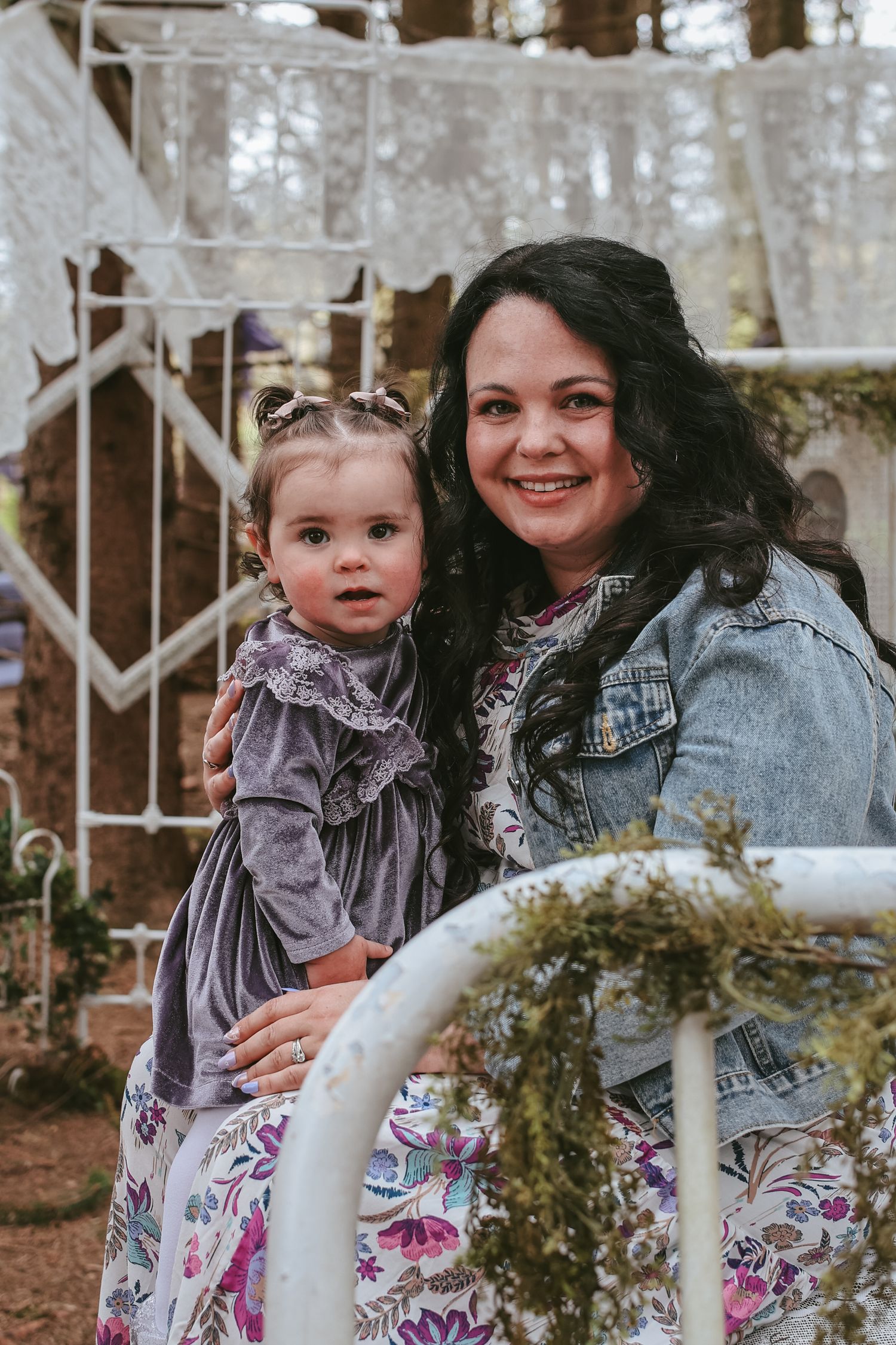 A parent and child pose together outdoors wearing matching floral dresses and denim, creating a sweet family moment.