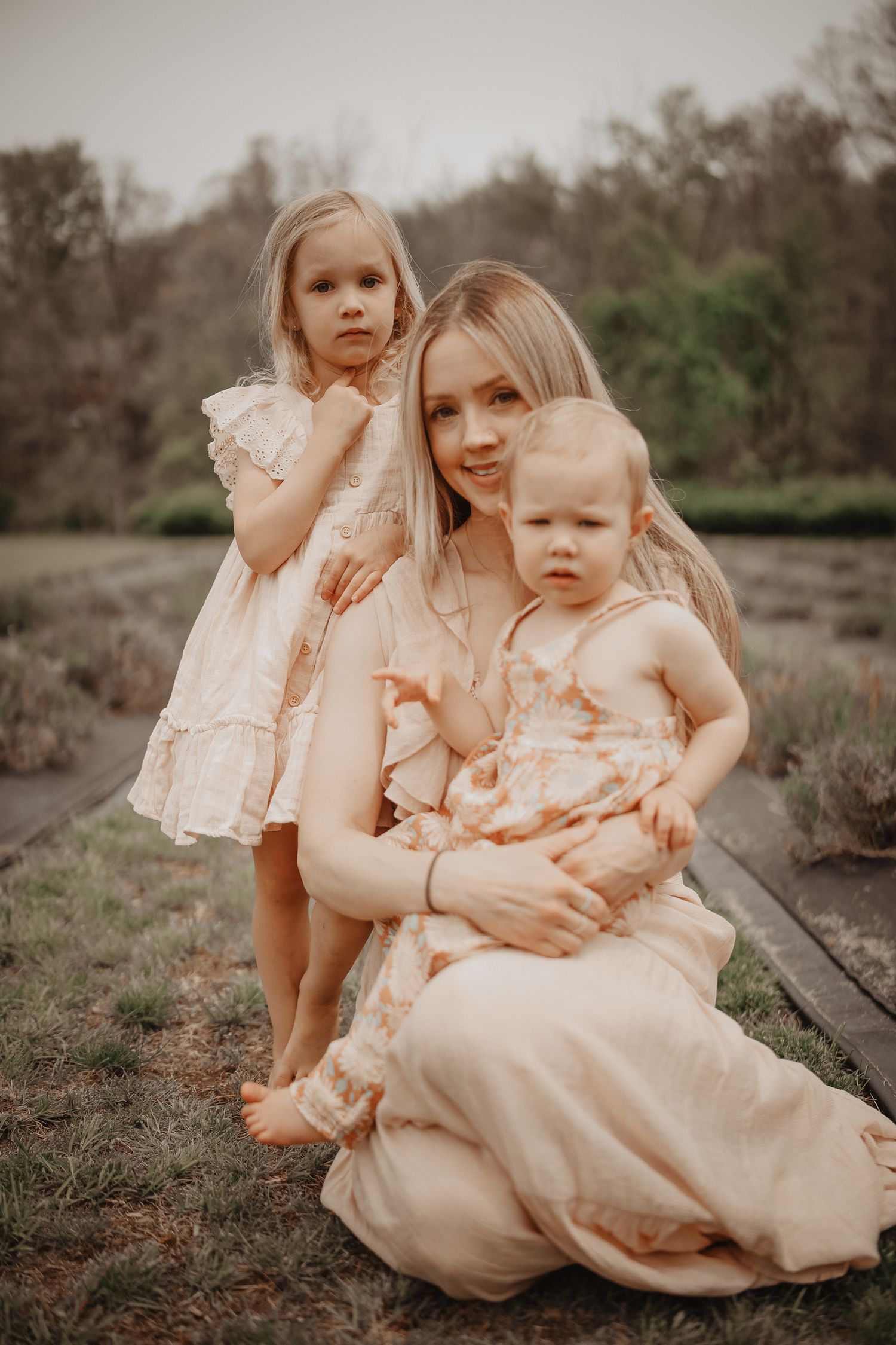 A family wearing matching peach-colored dresses poses together outdoors in a rustic natural setting.
