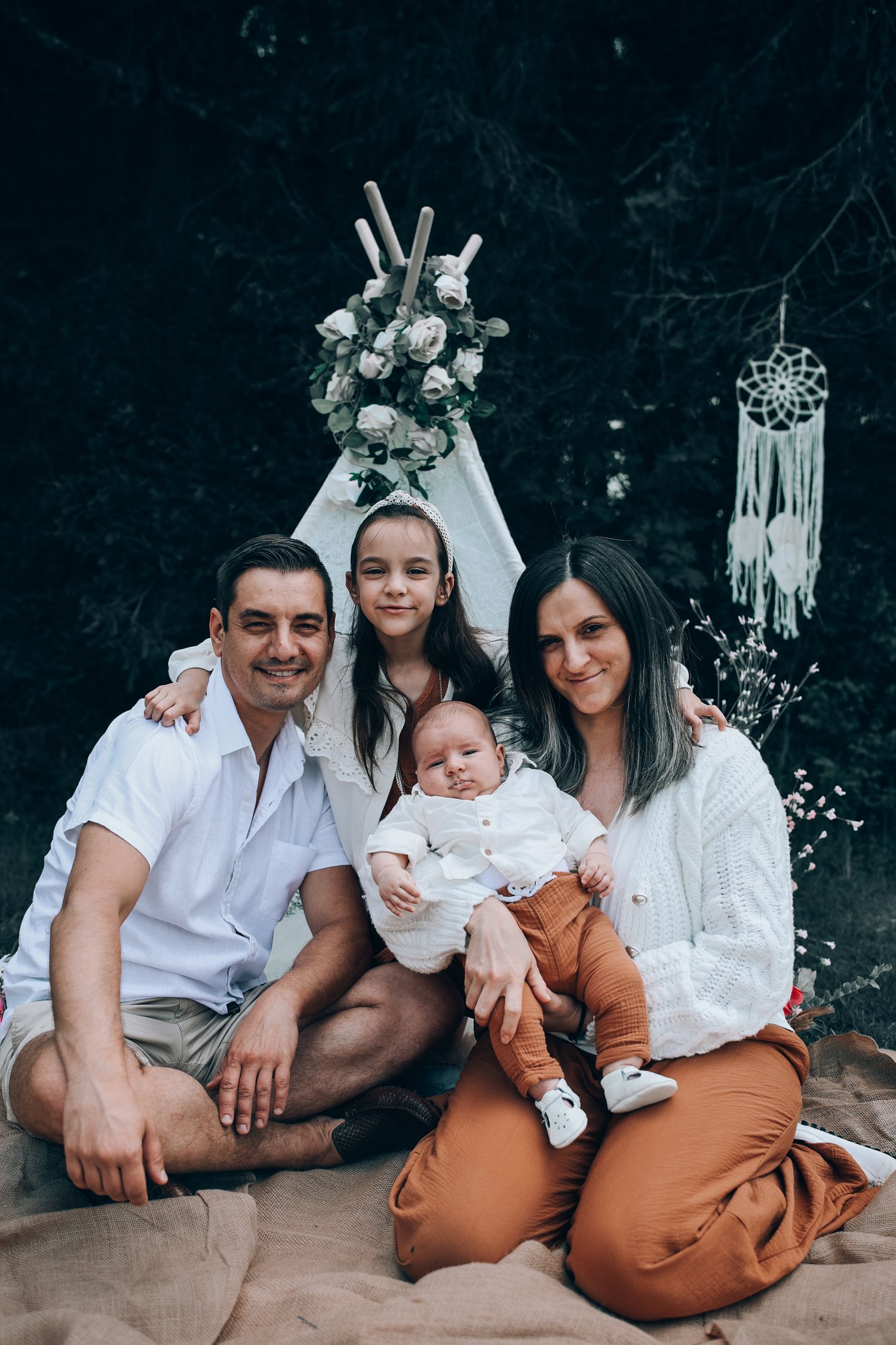 Family wearing coordinated white and rust-colored outfits poses together outdoors for casual portrait session.