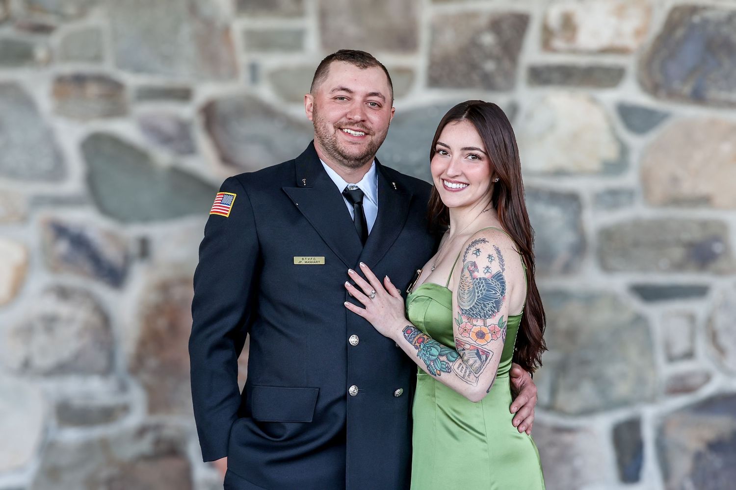 A couple poses together against a stone wall backdrop in formal and casual attire.