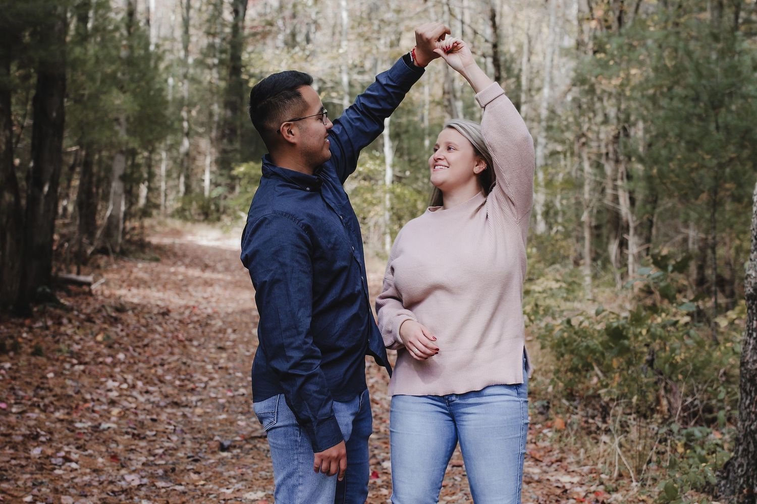A couple shares joyful moments while walking together through a peaceful autumn forest path.
