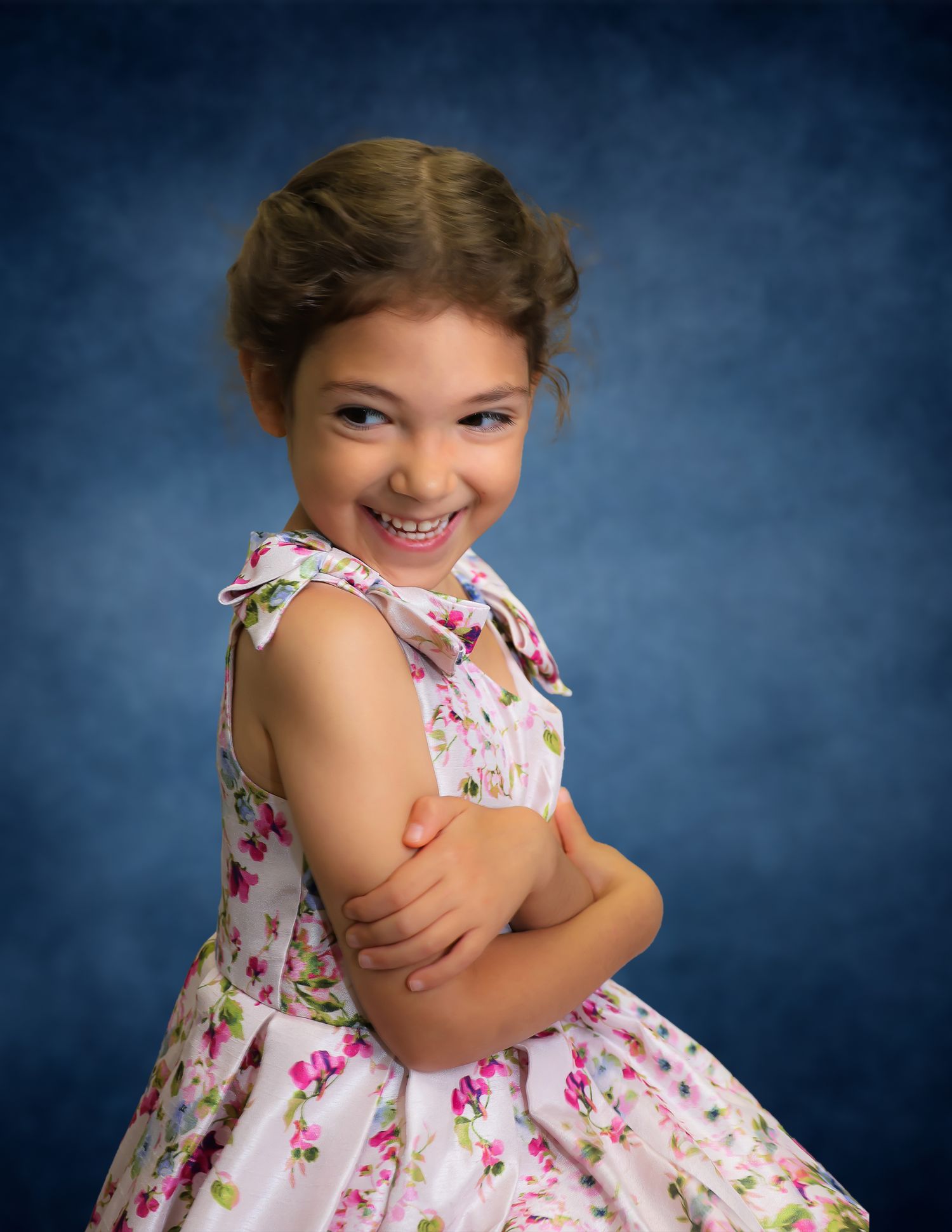 Young girl in floral dress smiling over shoulder, professional portrait with blue background.