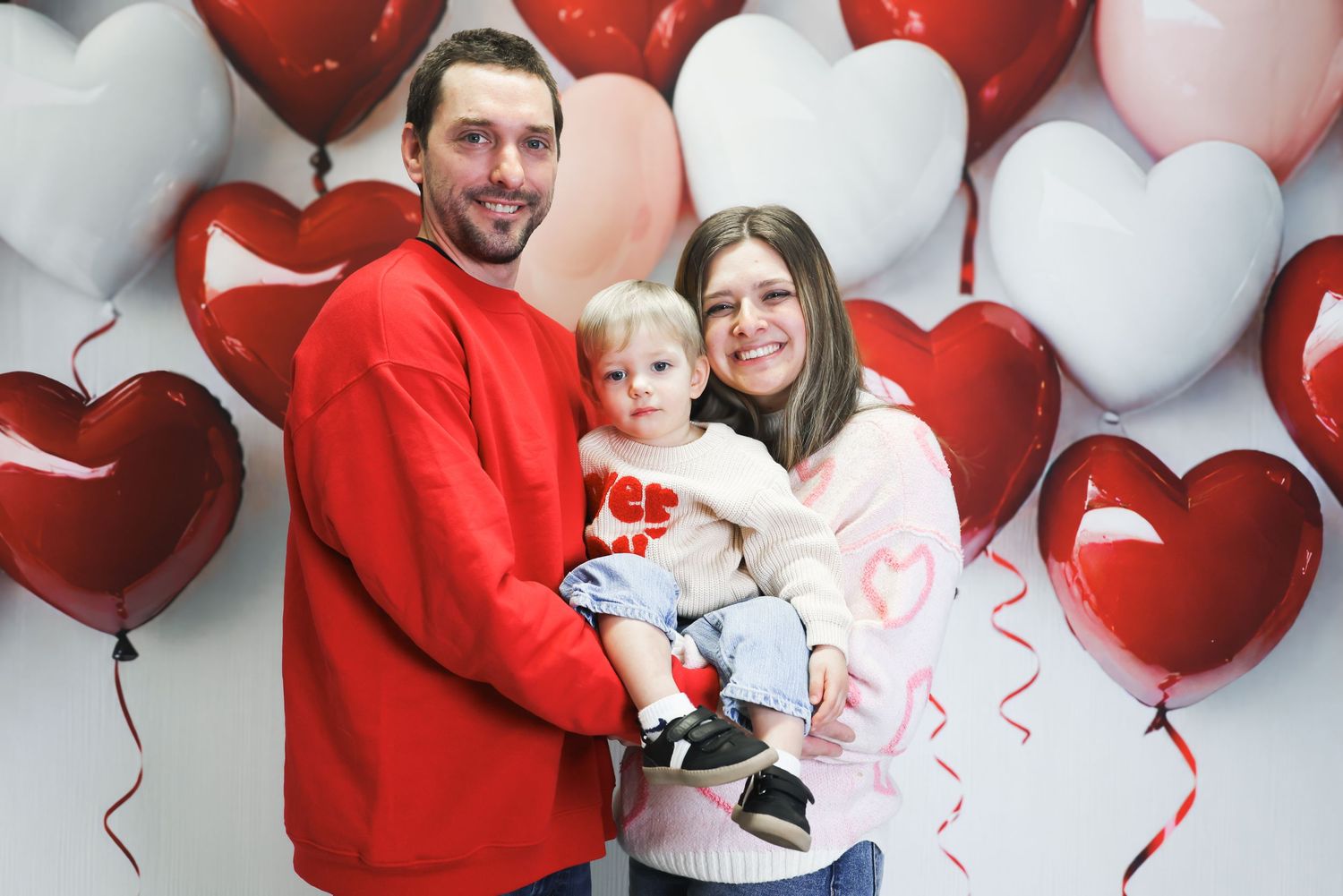 A happy family poses with red and pink heart balloons for a Valentine's Day photo shoot.