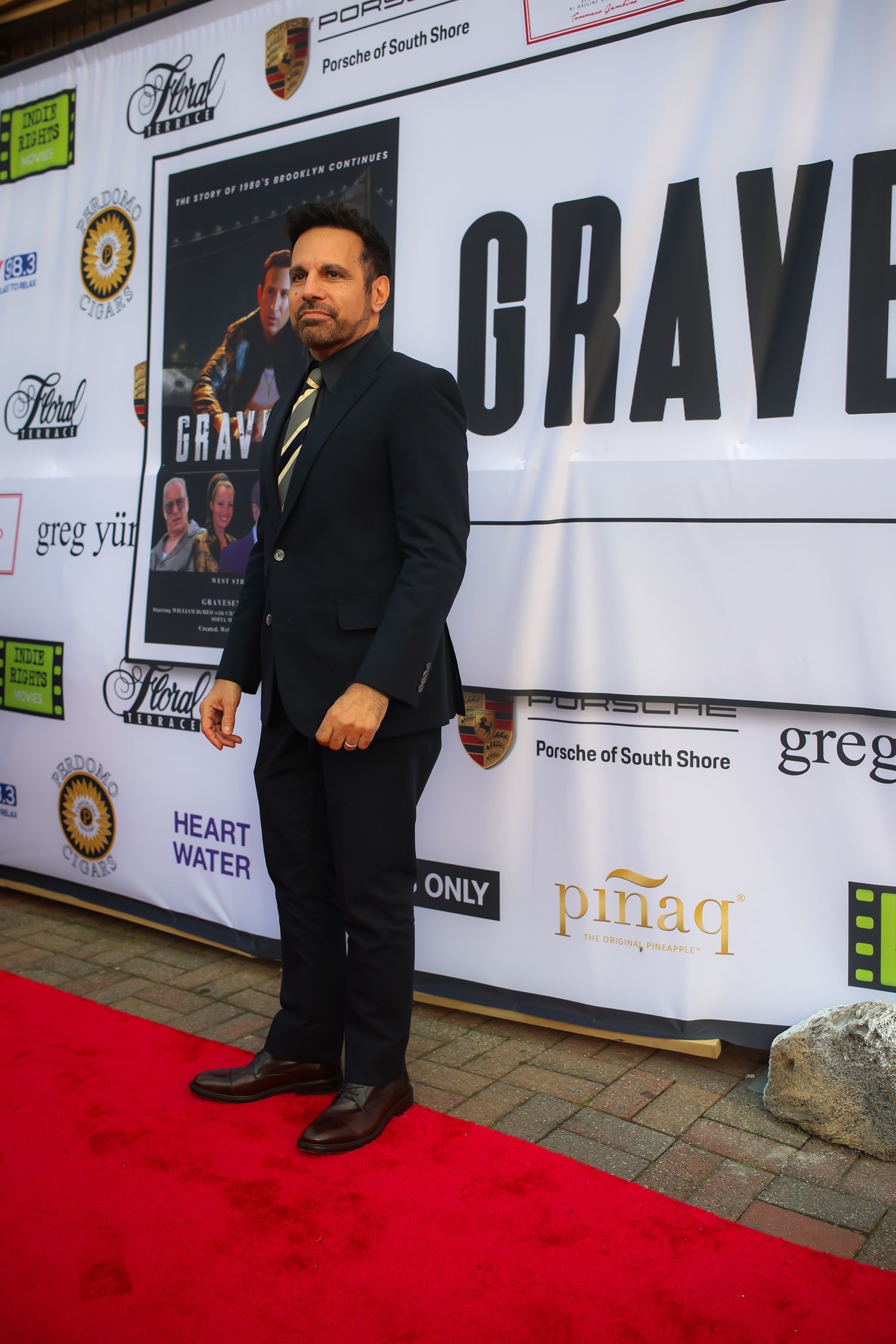 A person in a dark suit poses on a red carpet at a movie premiere event with 'GRAVE' signage visible in the background.