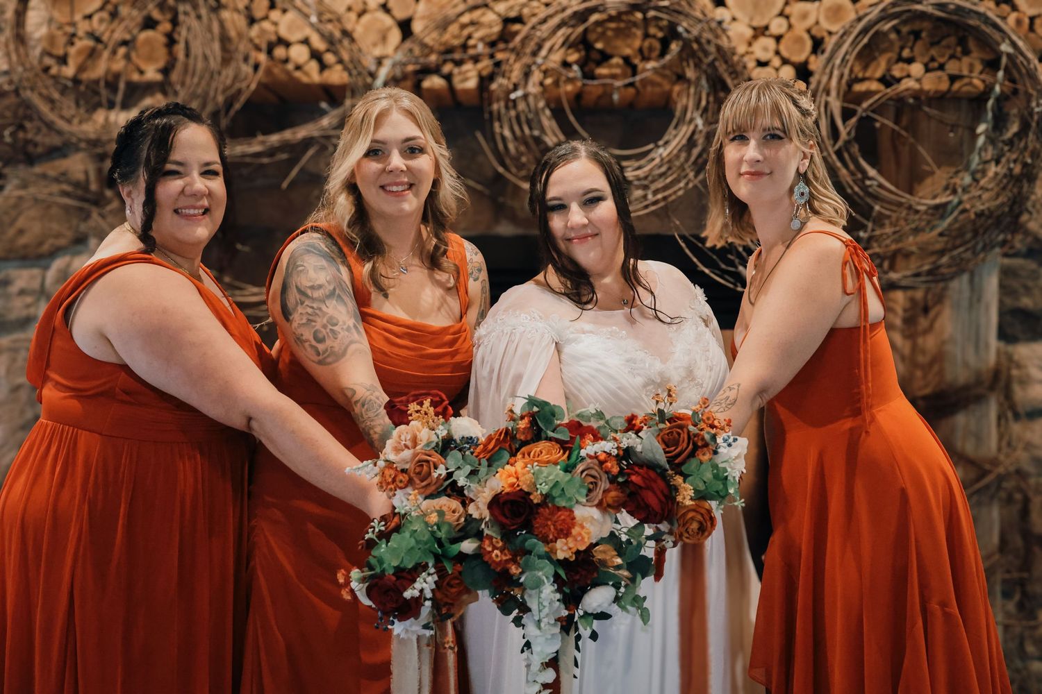 A wedding party wearing bright orange bridesmaid dresses poses together in an outdoor setting with floral bouquets.