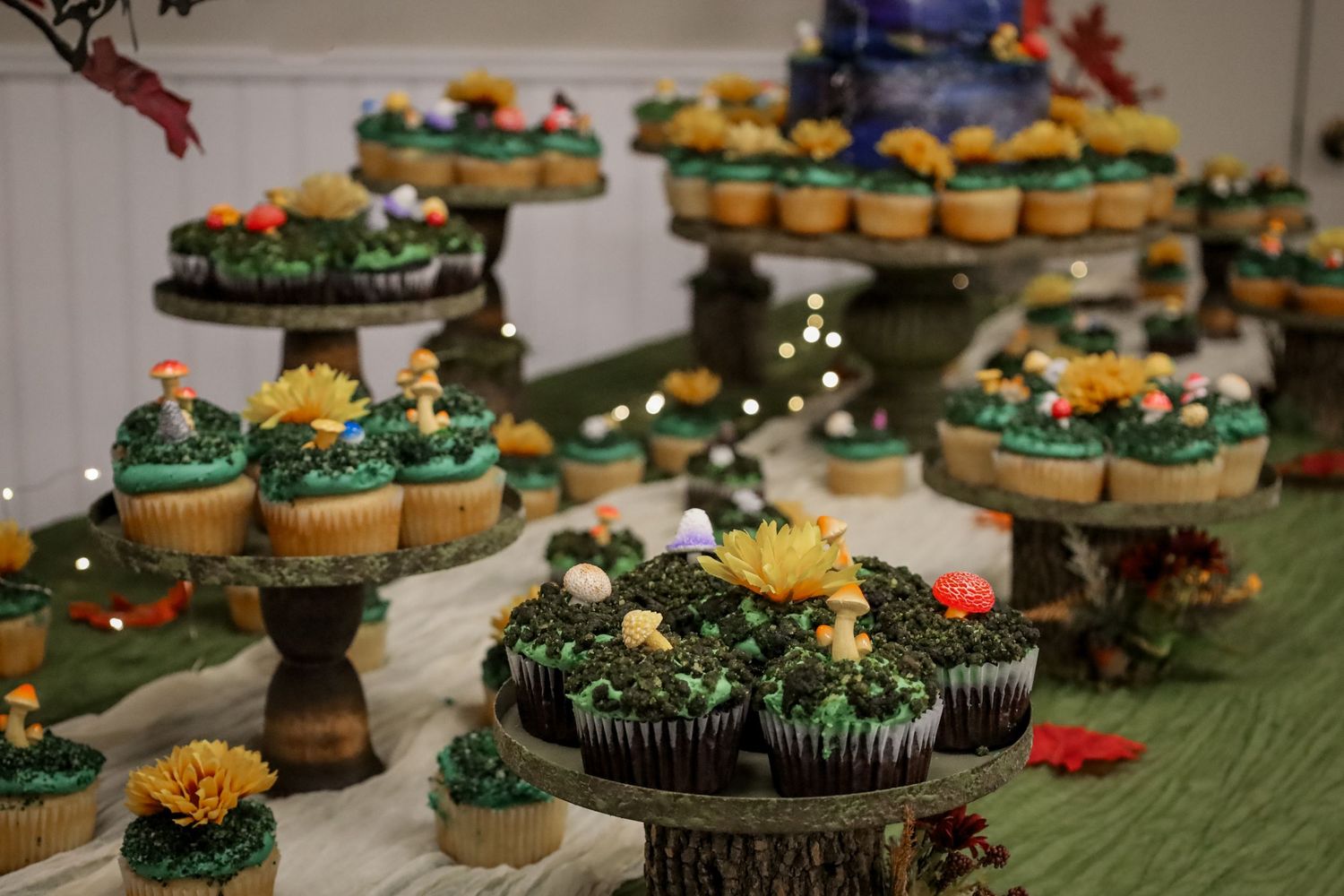 Green and yellow decorated cupcakes arranged on black cake stands with floral accents for a party display.