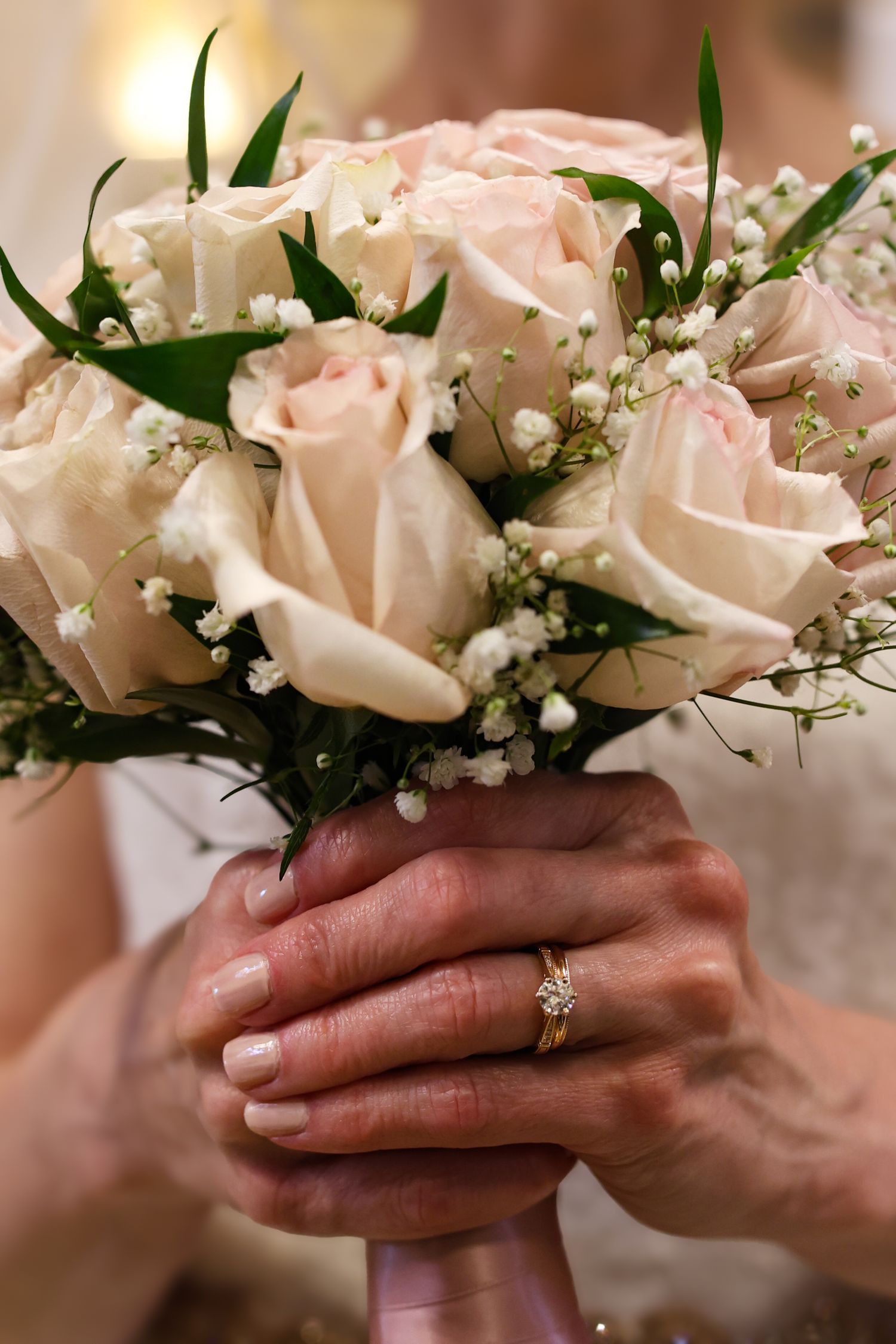 A close-up sequence of hands wearing an engagement ring with delicate pink roses and baby's breath flowers in the background.