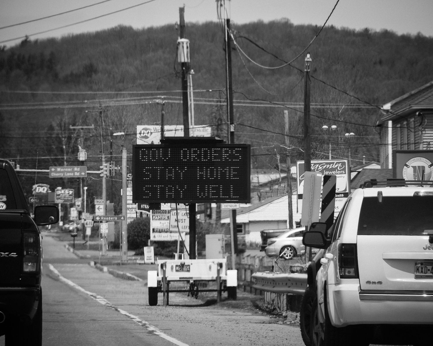 Digital road sign displaying 'Stay Home' message on a busy street with vehicles and power lines.