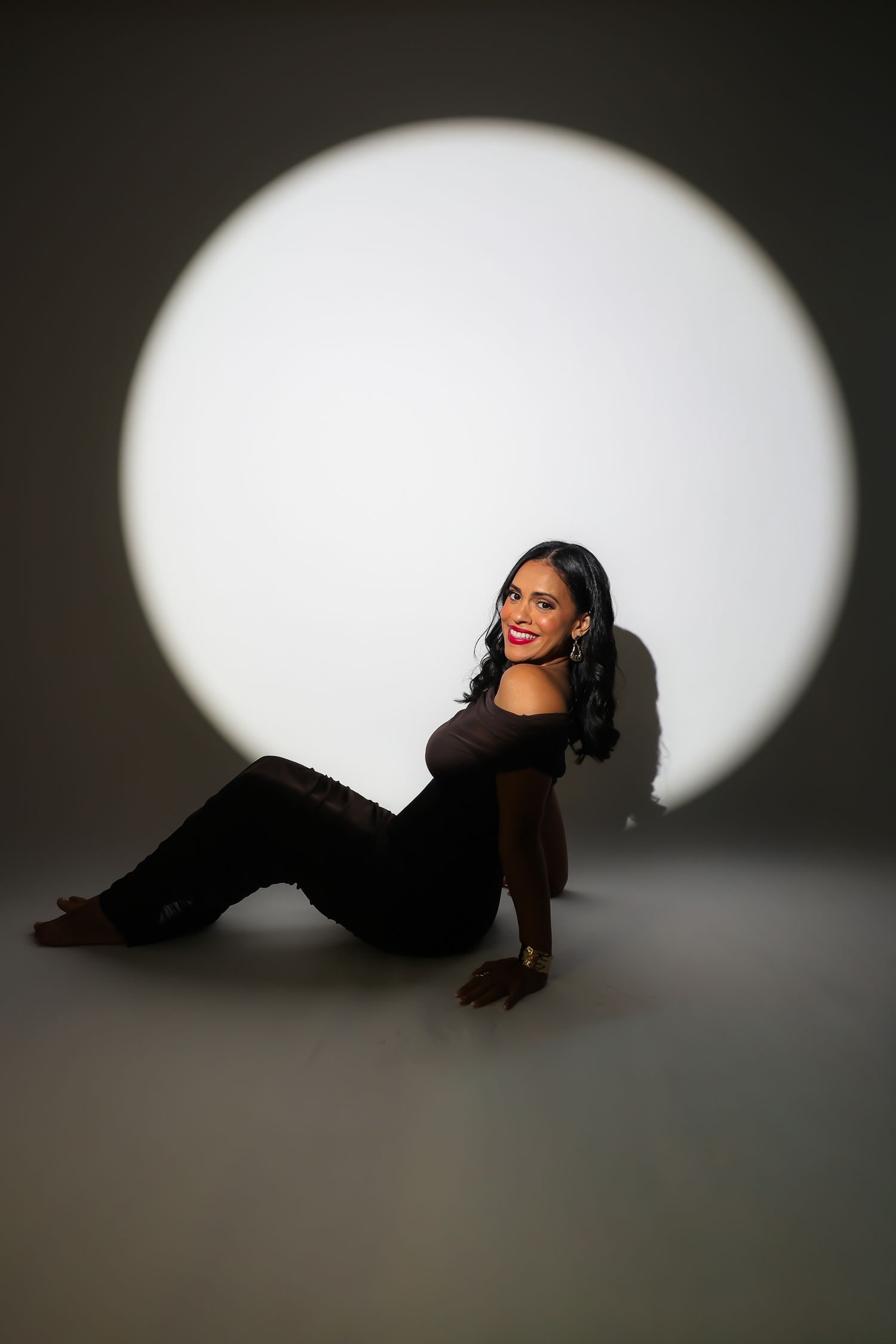 Fashion model in a black outfit poses against white spotlight backdrop creating dramatic silhouettes.