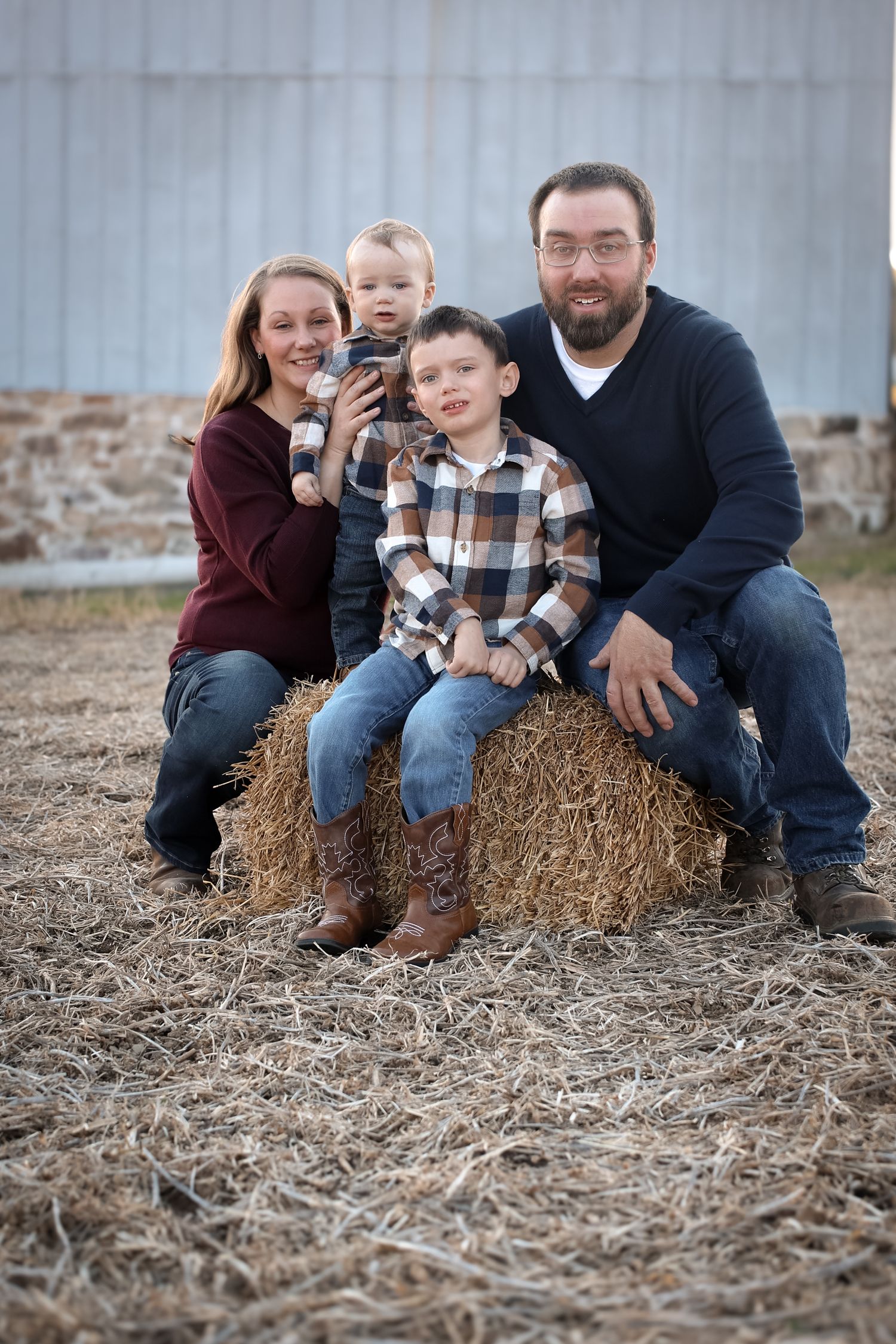 A family sits together on hay bales in a rustic outdoor setting during a casual photo session.