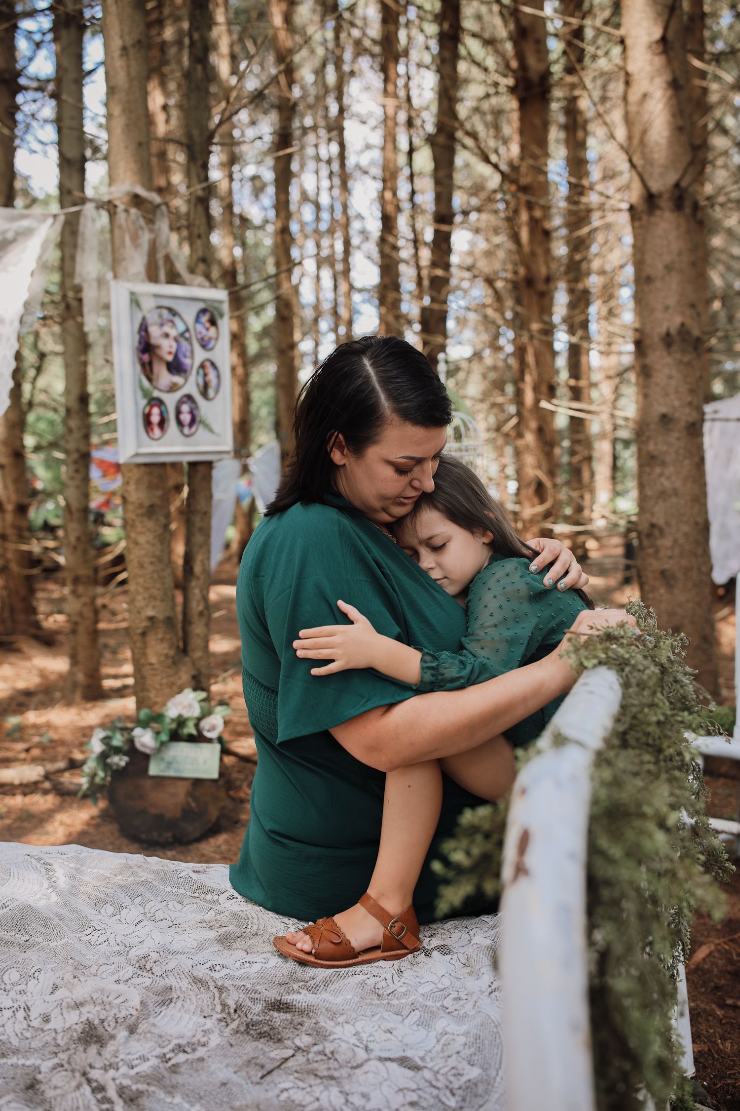 A couple shares tender embraces while sitting on rocks in a serene forest setting with photos displayed on trees.