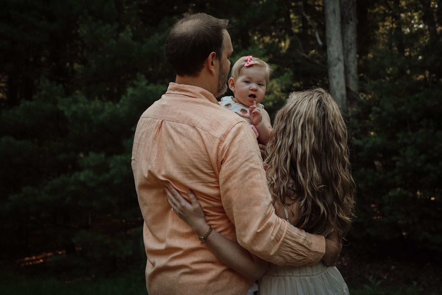 A couple in matching peach-colored outfits embraces while walking through a wooded area at sunset.
