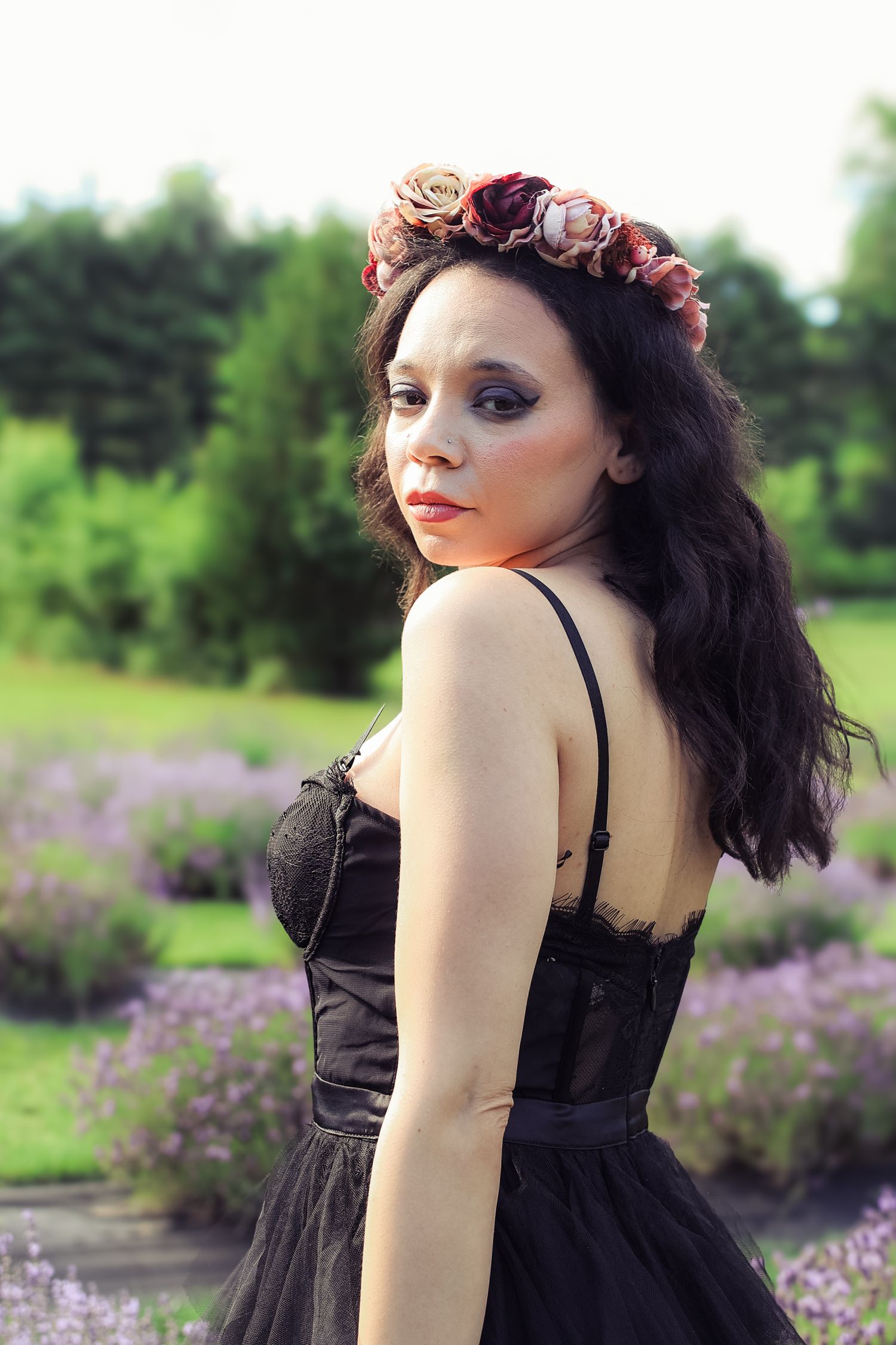 A woman in a black dress poses gracefully in a field of purple wildflowers on a summer day.