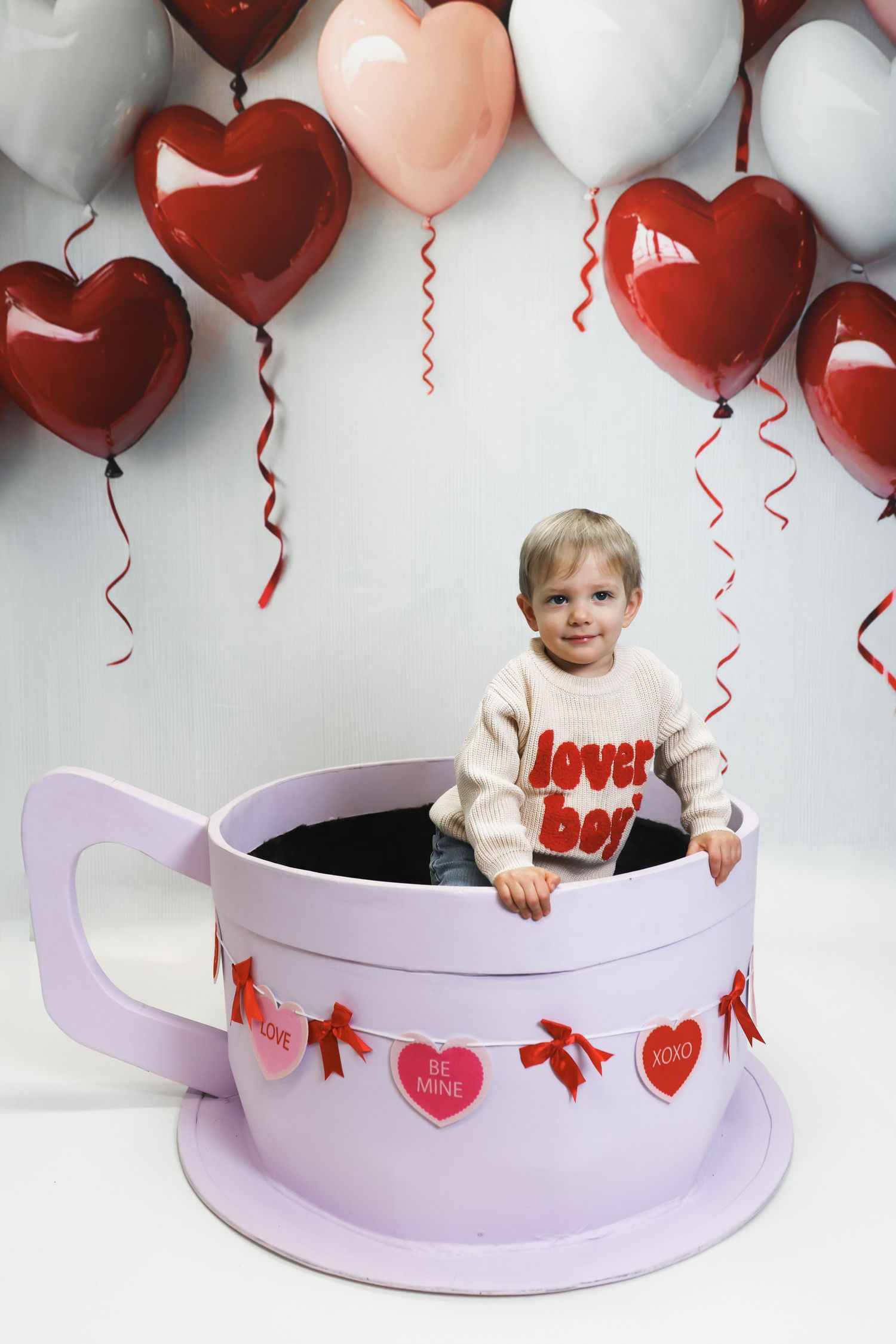 A Valentine's themed photo series showing a pink teacup prop with heart balloons and decorations in the background.